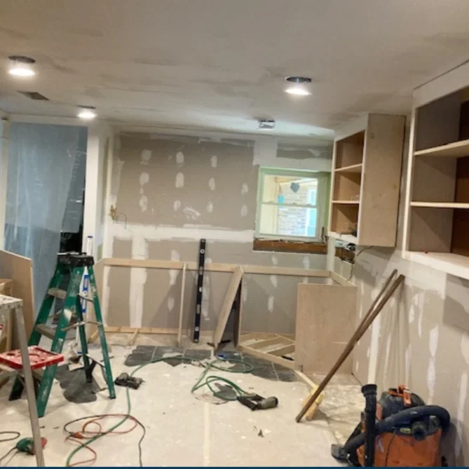 Interior view of a basement or room under renovation, with unfinished drywall, construction tools, a step ladder, and open shelves.