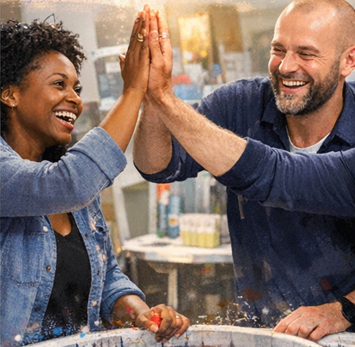 Two people celebrating with a high five, smiling in a workspace or creative studio.