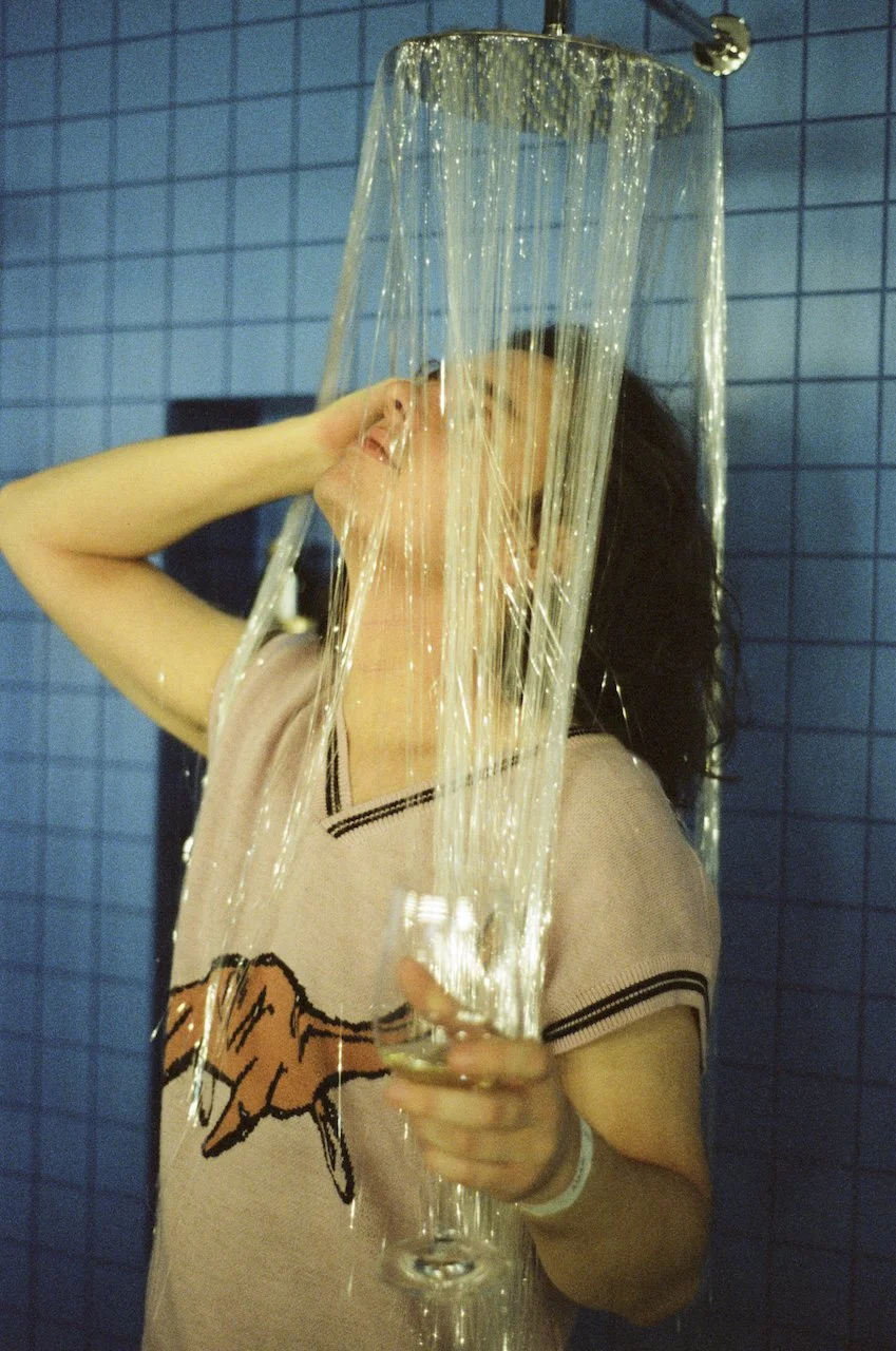 Junge Frau steht unter einer riesigen Wasserfall-Dusche mit Wasser, das direkt aus der Duschköpfe fällt, im Badezimmer mit blauen Fliesen.