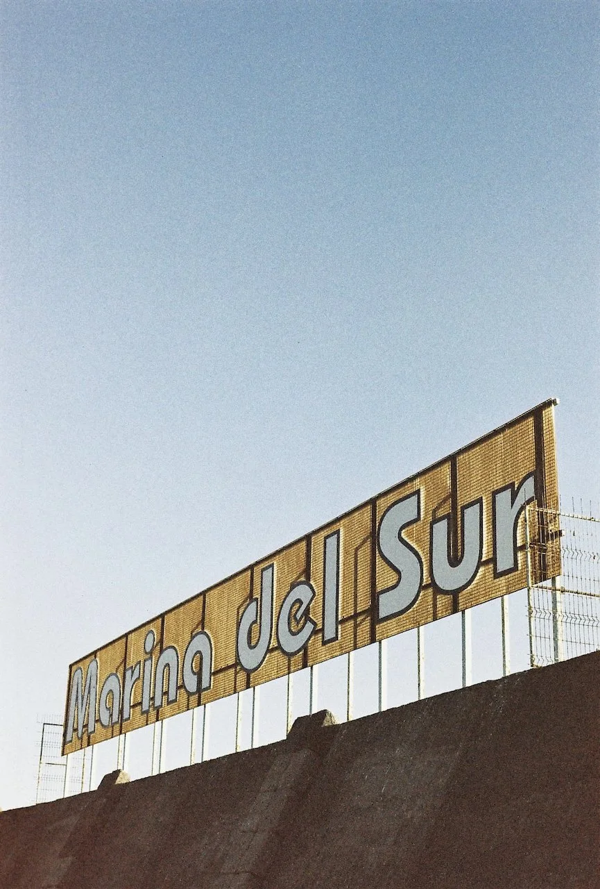 Ein gelschild mit der Aufschrift 'Marina di Sur' auf einer Mauer, gegen den blauen Himmel fotografiert.