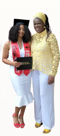Two women standing together, one in a graduation cap and gown holding a diploma, the other in a yellow top and white pants, smiling at the camera.