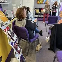 A group of people sitting in chairs in a store, browsing displays, with a cat on the floor nearby.