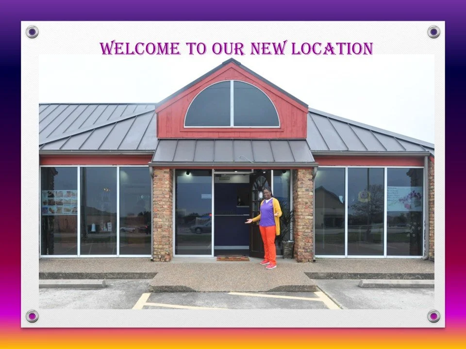 A woman standing outside a new building with a sign that says 'Welcome to our new location'.