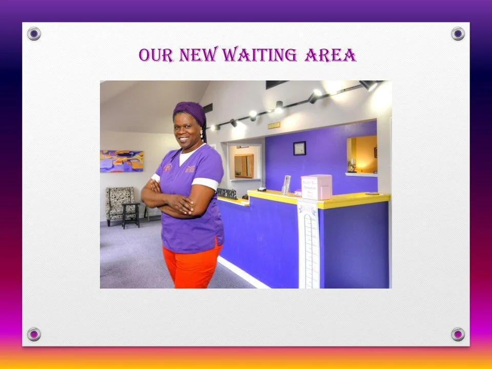 A woman in purple scrubs and orange pants standing in a new waiting area with a reception desk, colorful wall, and seating.