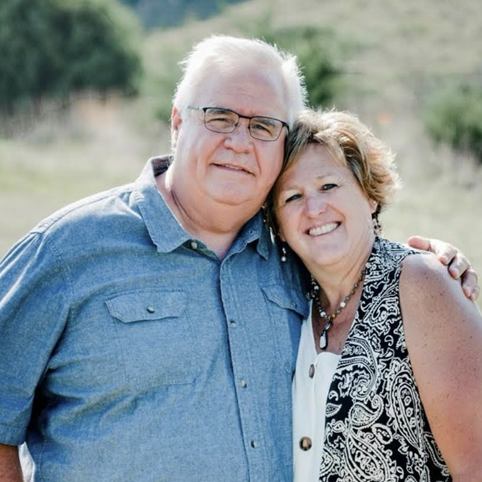 A happy older man and woman smiling and hugging outdoors in a rural setting.
