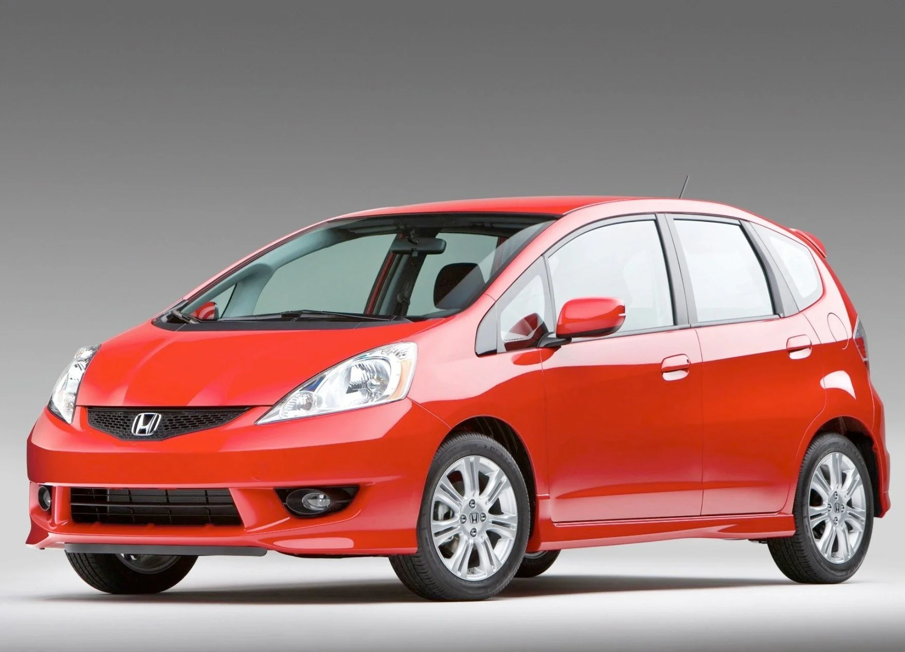 Red Honda Fit compact hatchback car on a plain gray background.