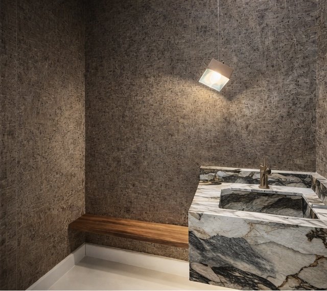 A small bathroom corner with textured gray walls, a marble sink with black, gray, and white veins, a wooden bench, and a modern angled ceiling light.
