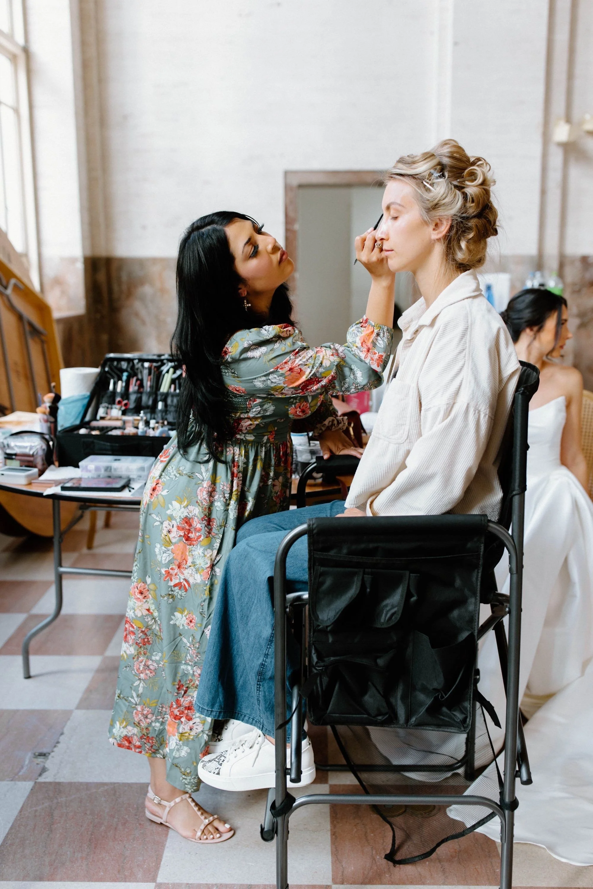 Florida Makeup artist applying makeup to a woman in a wheelchair, with another woman in white dress sitting in the background.