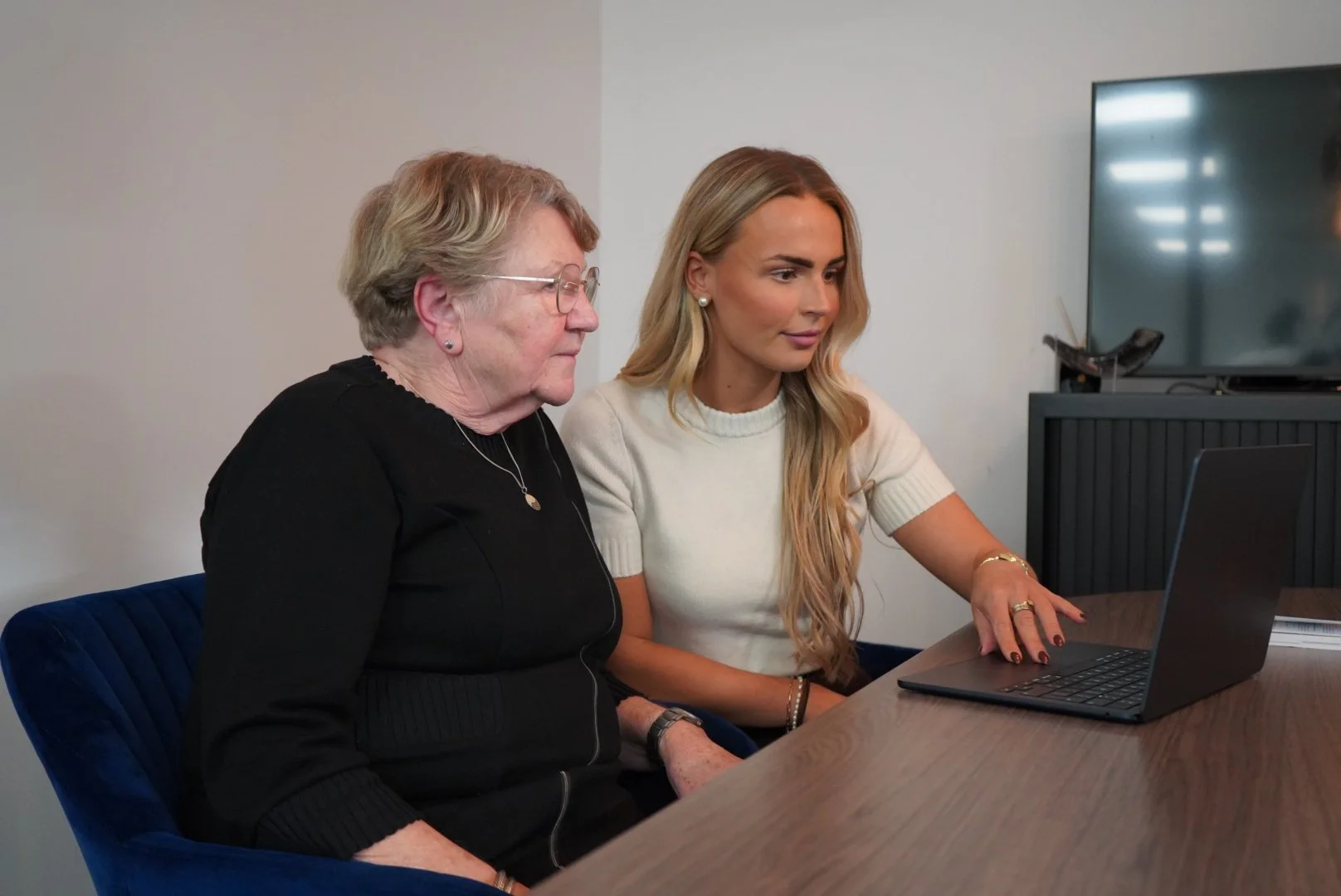 Twee vrouwen zitten samen voor een laptop, kijken naar het scherm.