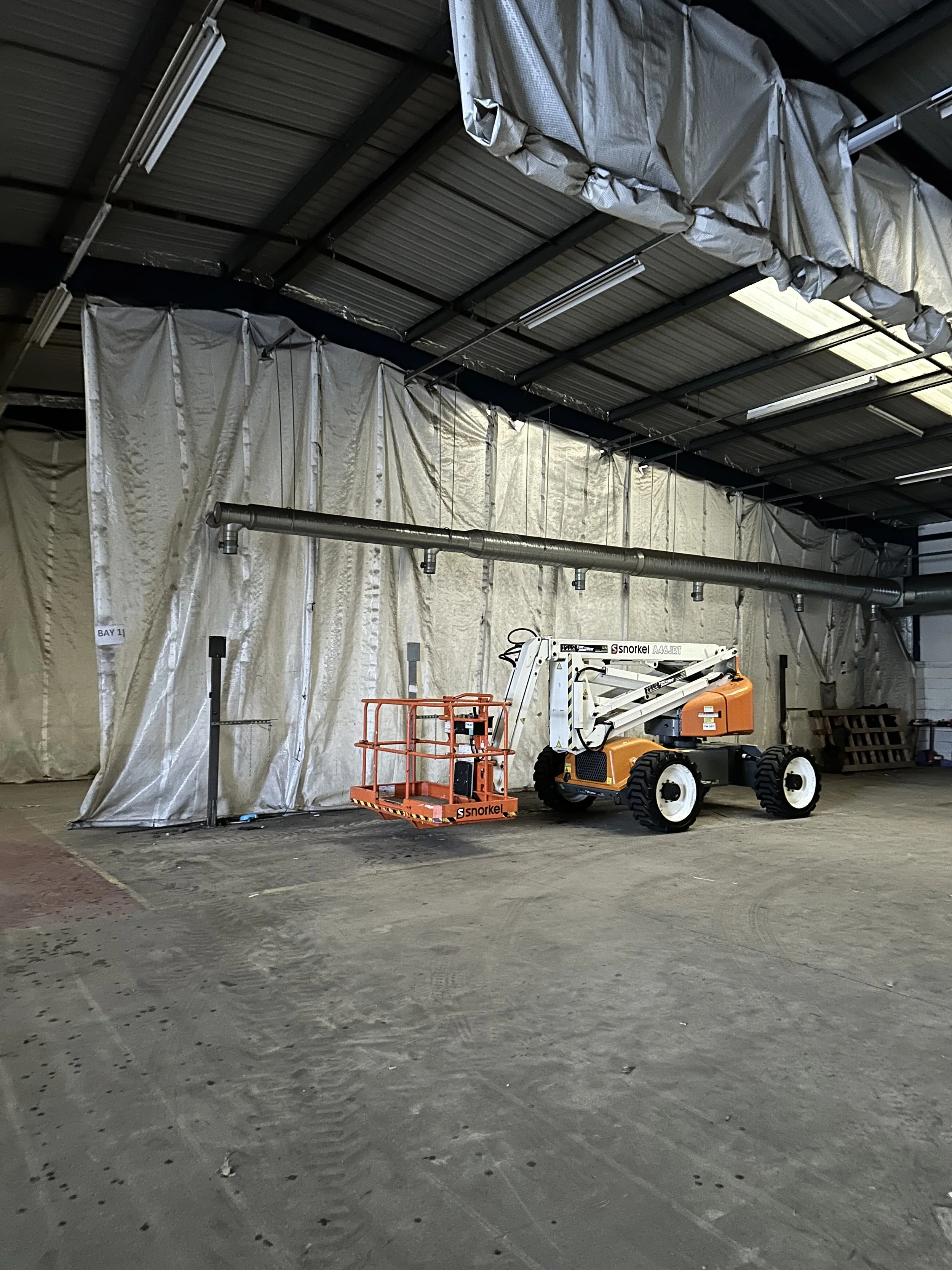 Interior of a warehouse with a Snorkel boom lift parked on a concrete floor, and beige tarps covering the walls and ceiling.