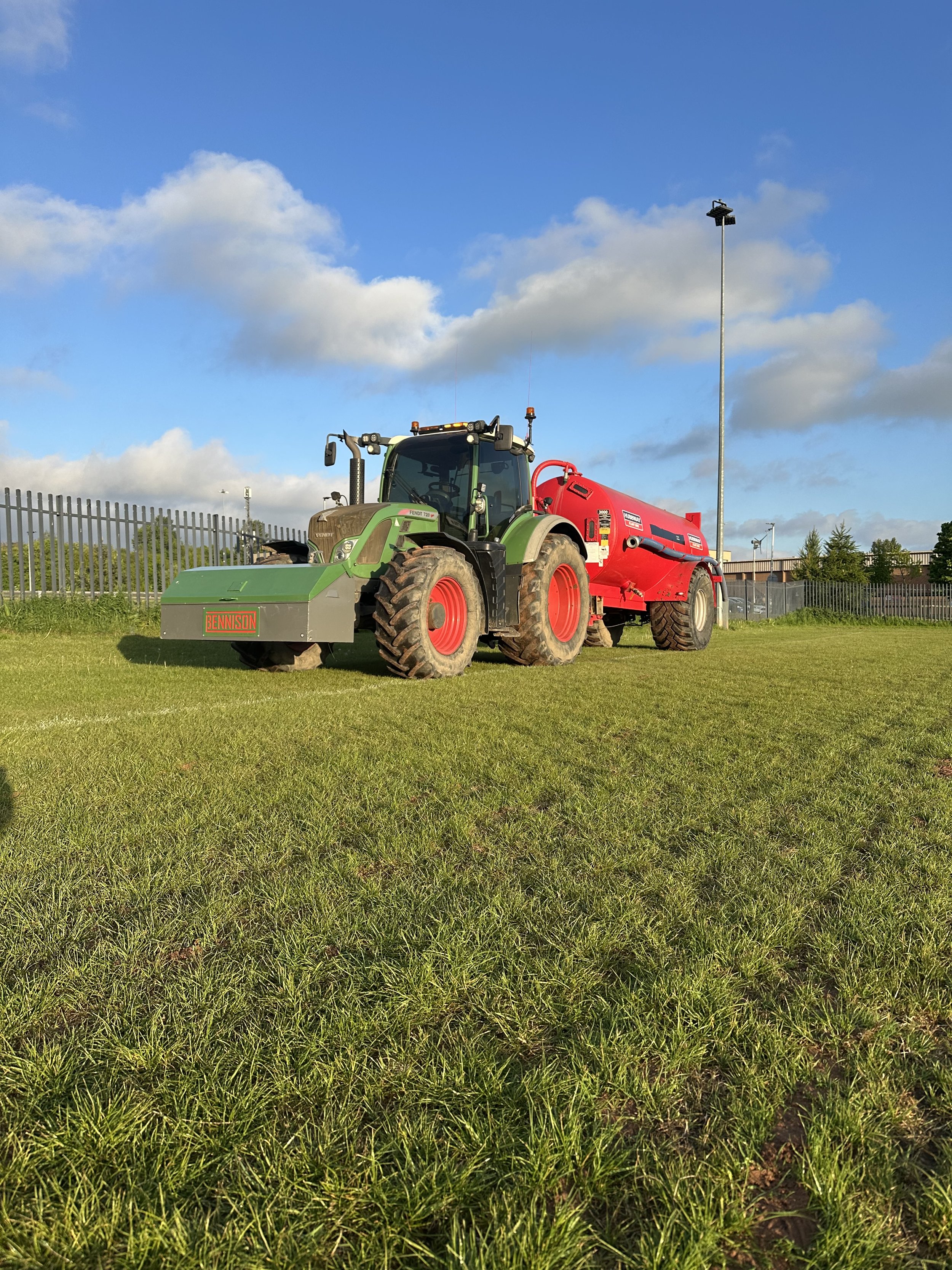 Green and red tractor on a grassy field under a blue sky with white clouds.