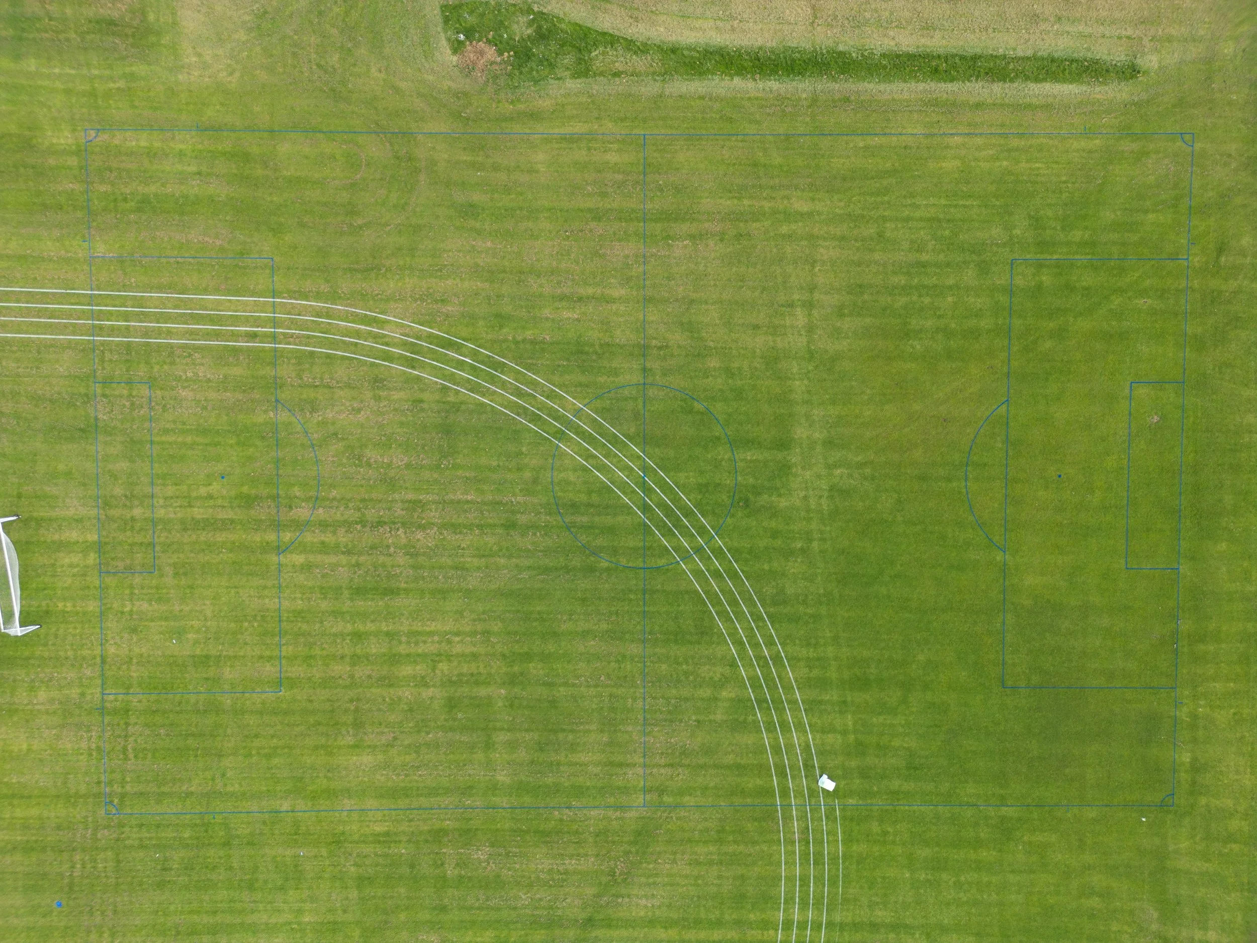 An aerial view of a sports field with marked court lines for soccer and running tracks, and a small portion of a goalpost visible on the left side.