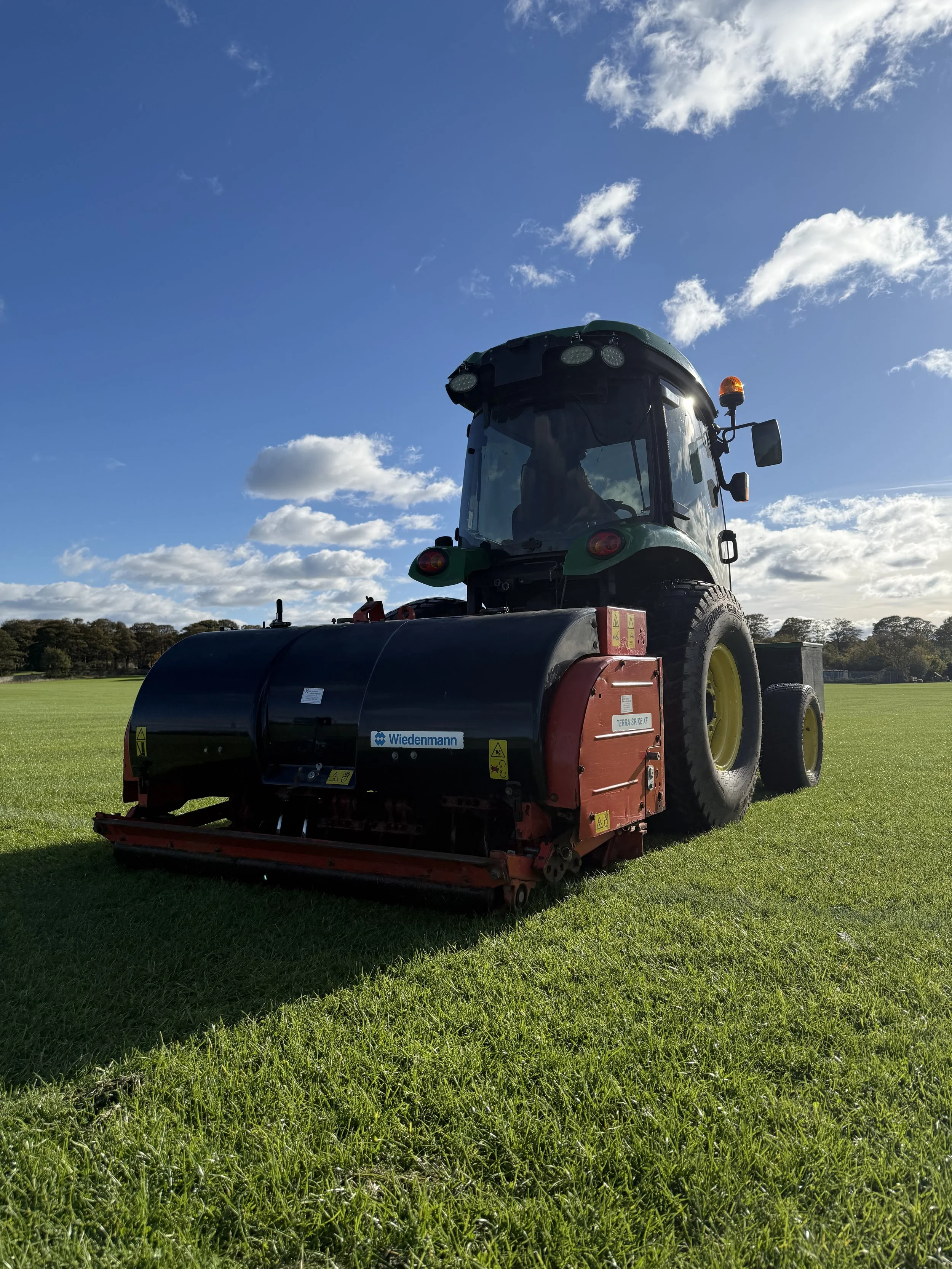 A large green and red tractor on a grassy field under a partly cloudy blue sky.