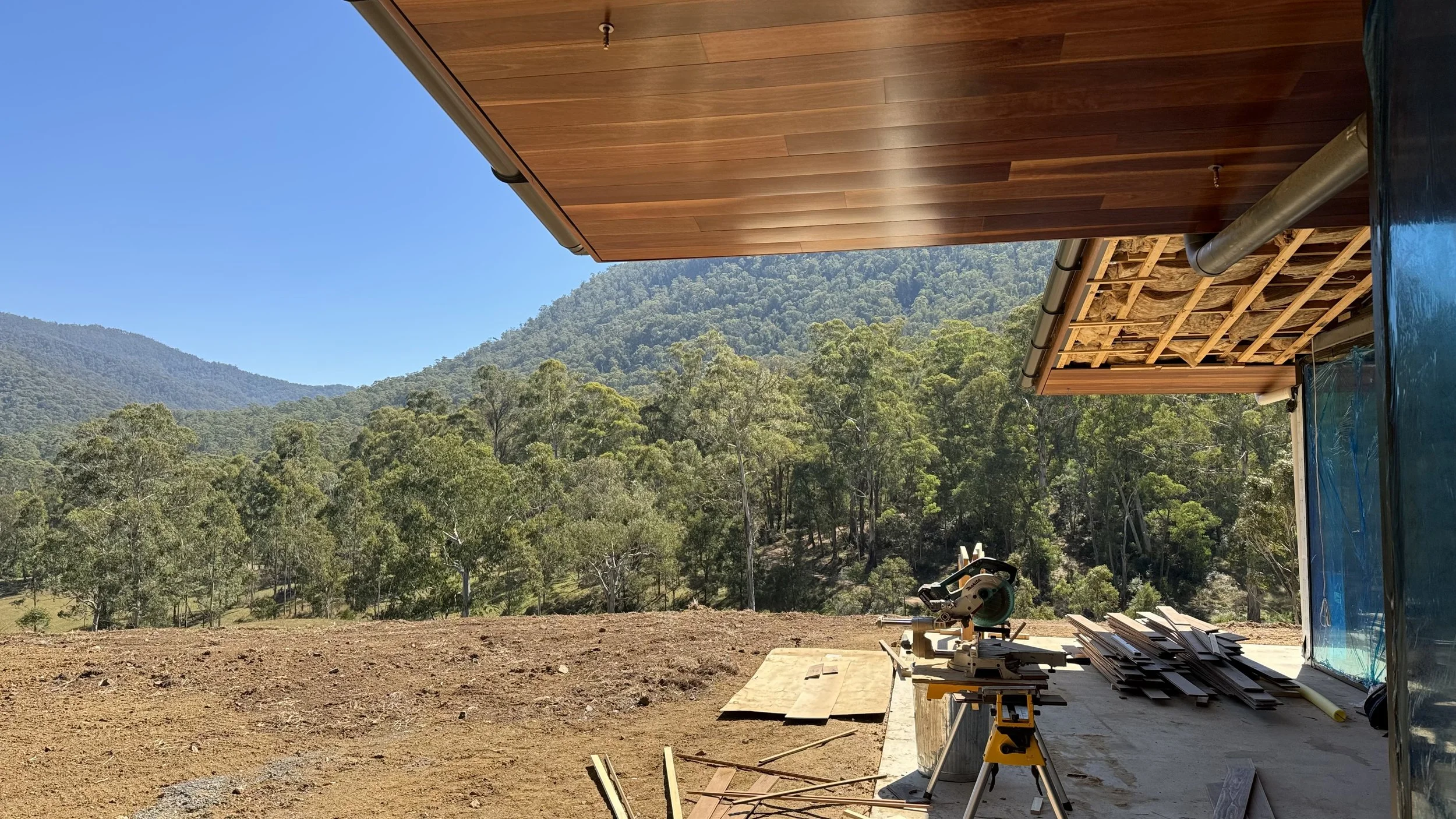 Construction site with partially built structure, wooden ceiling, and mountain view in the background.