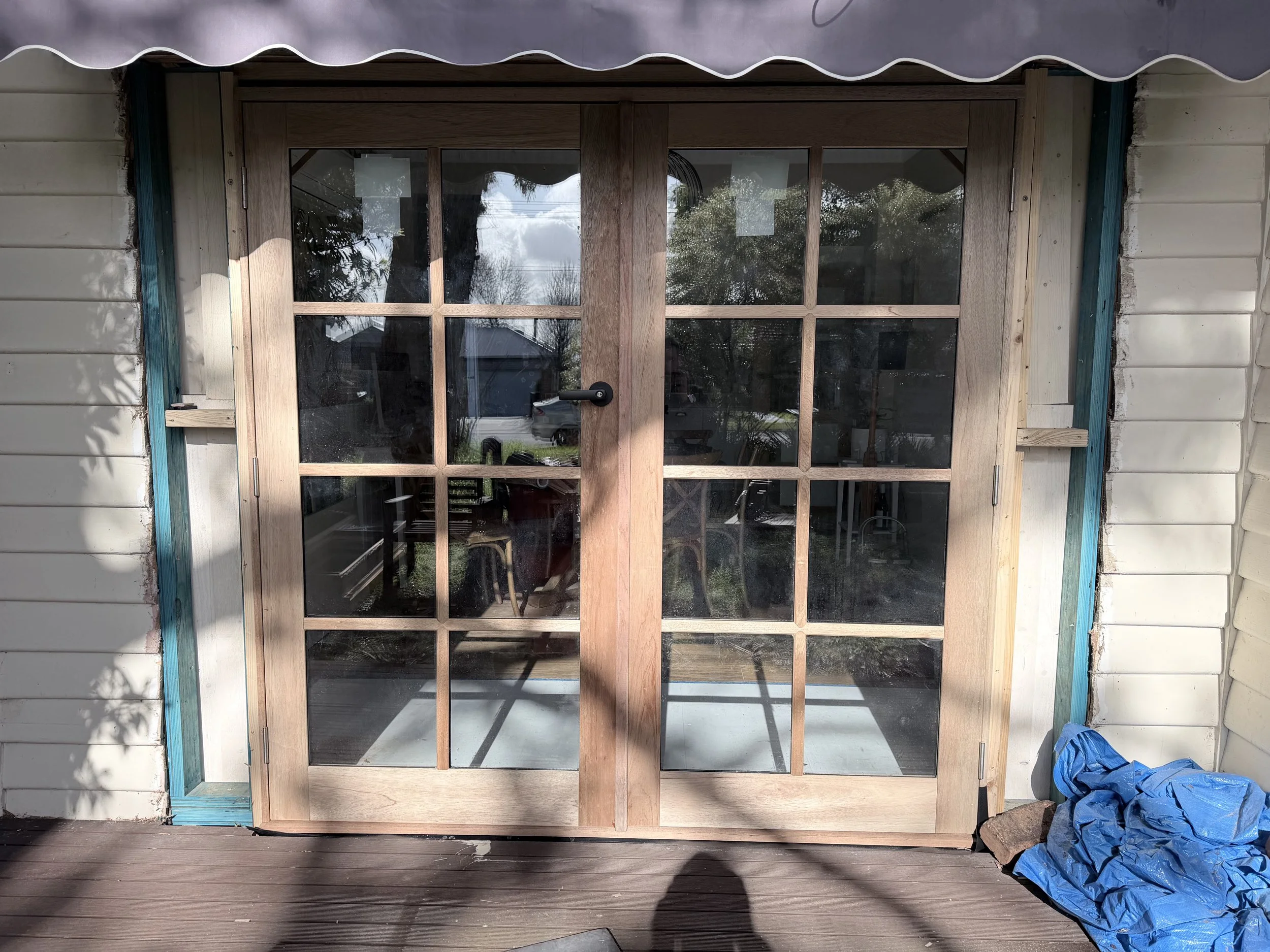 Wooden framed glass patio door installed in a house under construction, with a shadow of the person taking the photo visible on the wooden deck outside
