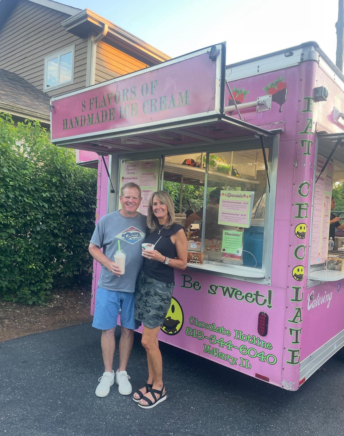 A man and woman standing in front of a pink ice cream truck, smiling and holding ice cream treats.