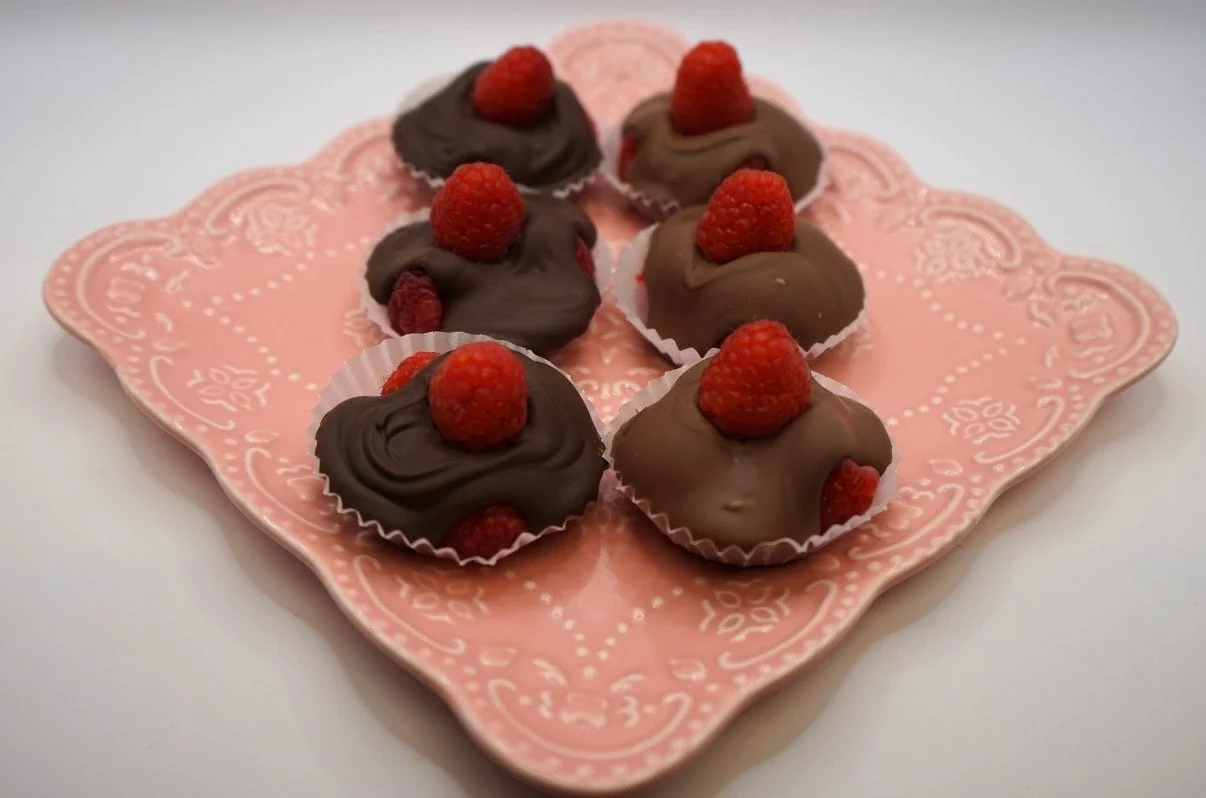 Six chocolates topped with raspberries on a pink decorative plate.