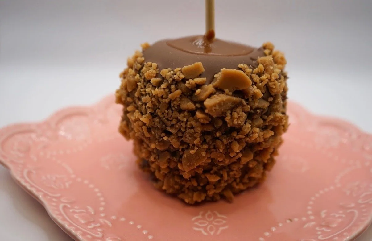 Caramel apple covered in crushed nuts on a pink decorative plate