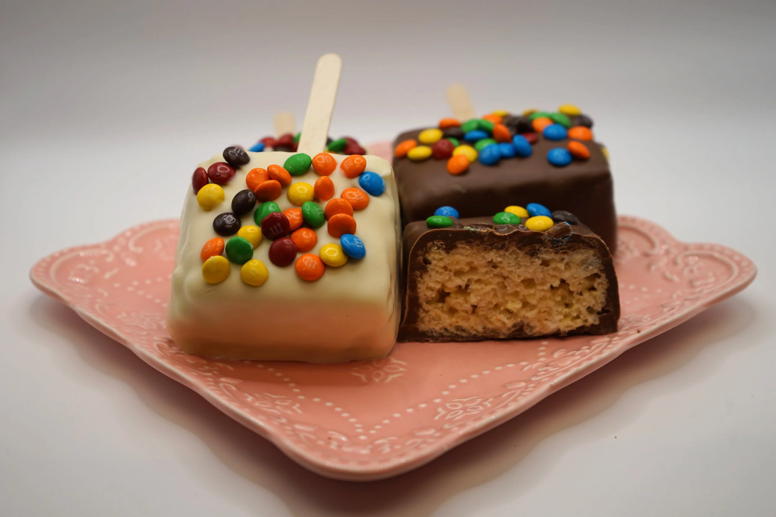 Three square pieces of cake with colorful candy sprinkles on top, served on a pink decorative plate.