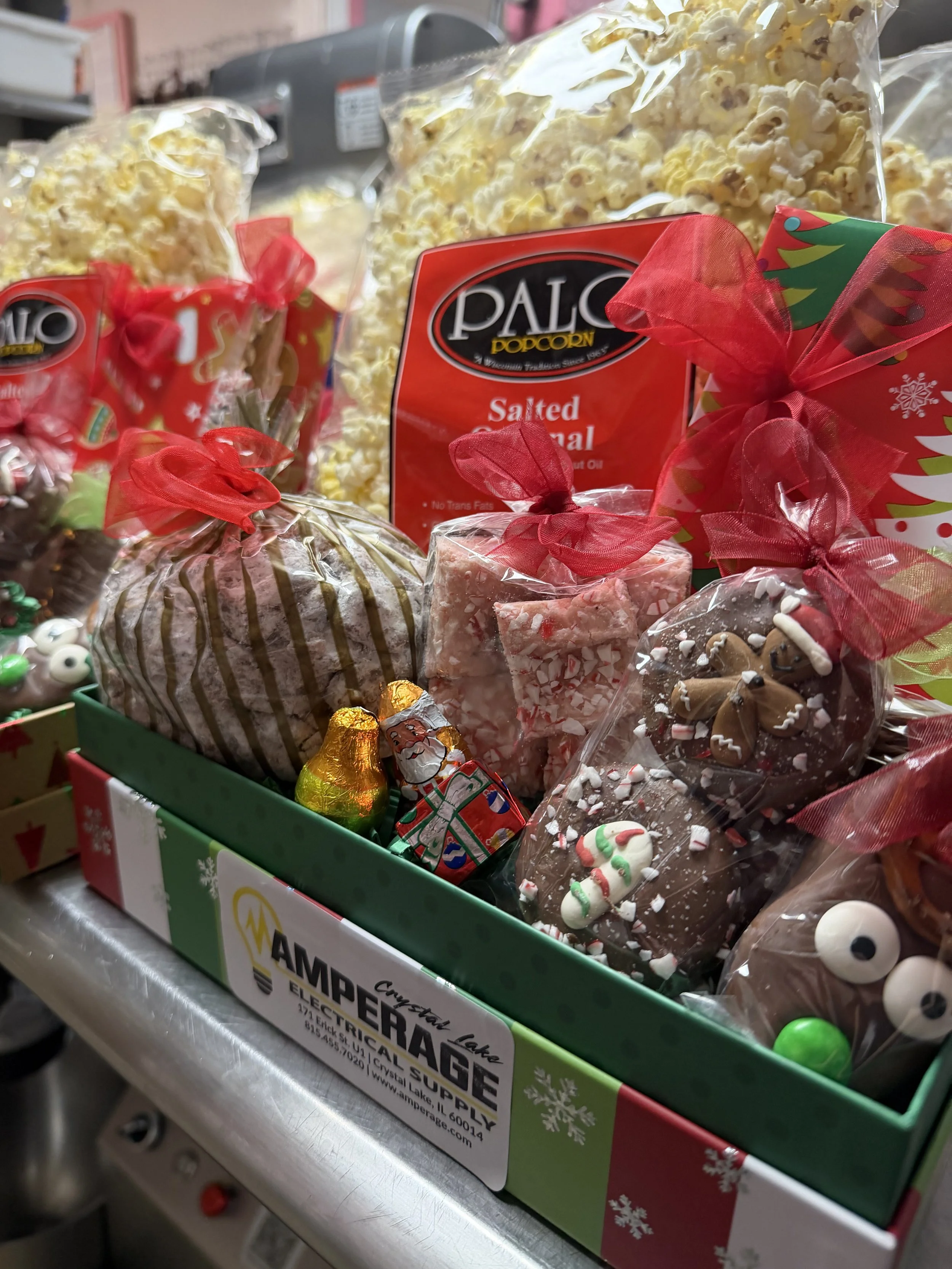 Christmas-themed gift box containing popcorn, candy, and chocolates, with red ribbons and holiday decorations.