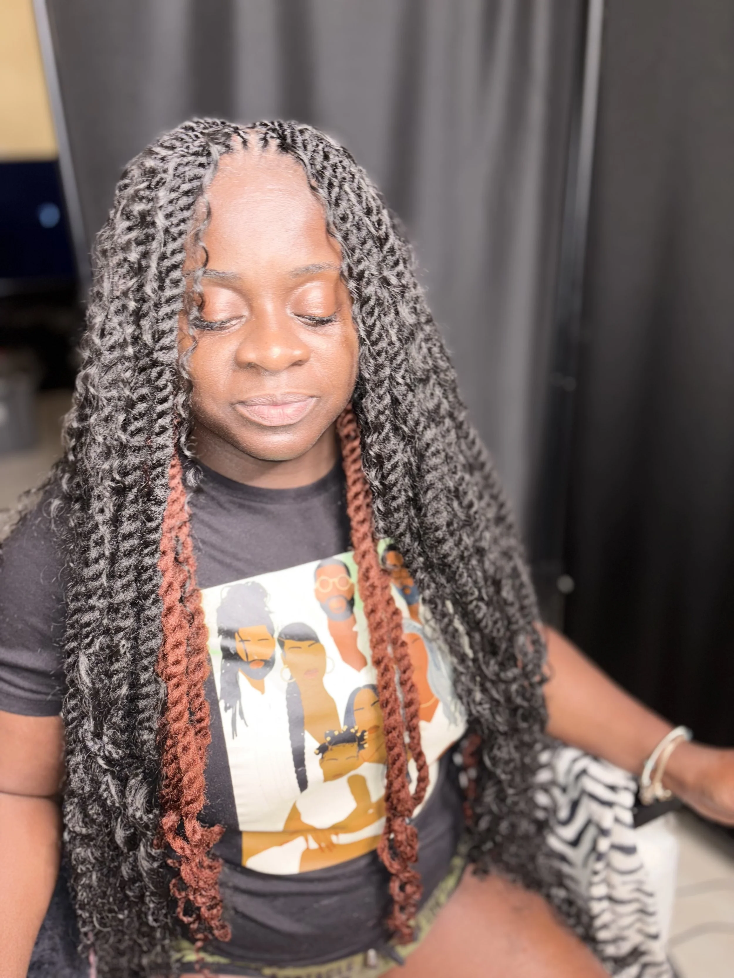A woman with twisted black and white hair wearing a black graphic T-shirt, sitting indoors with eyes closed.