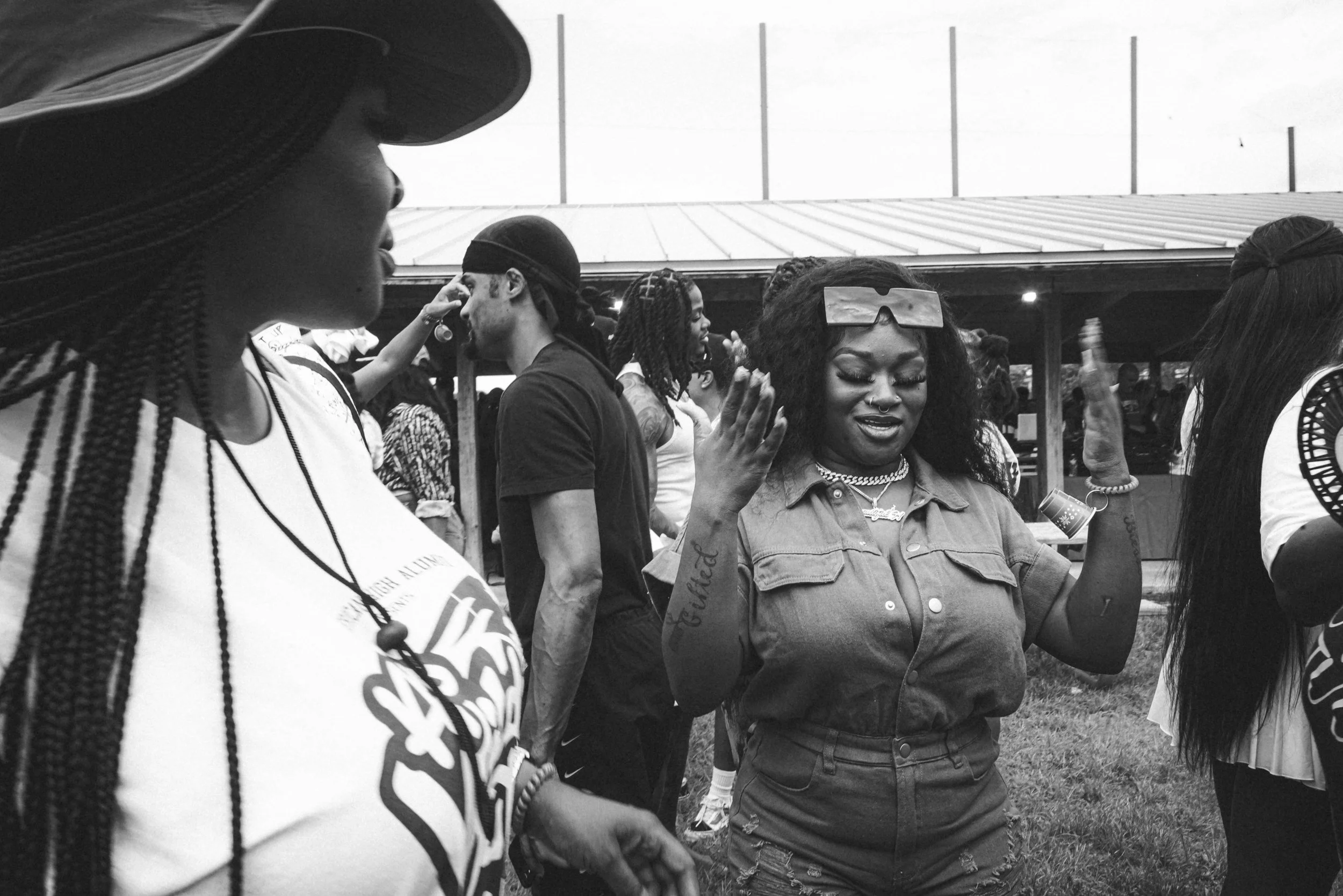 Group of women socializing outdoors at a festival or park in black and white, with some women engaging in conversation and others smiling.