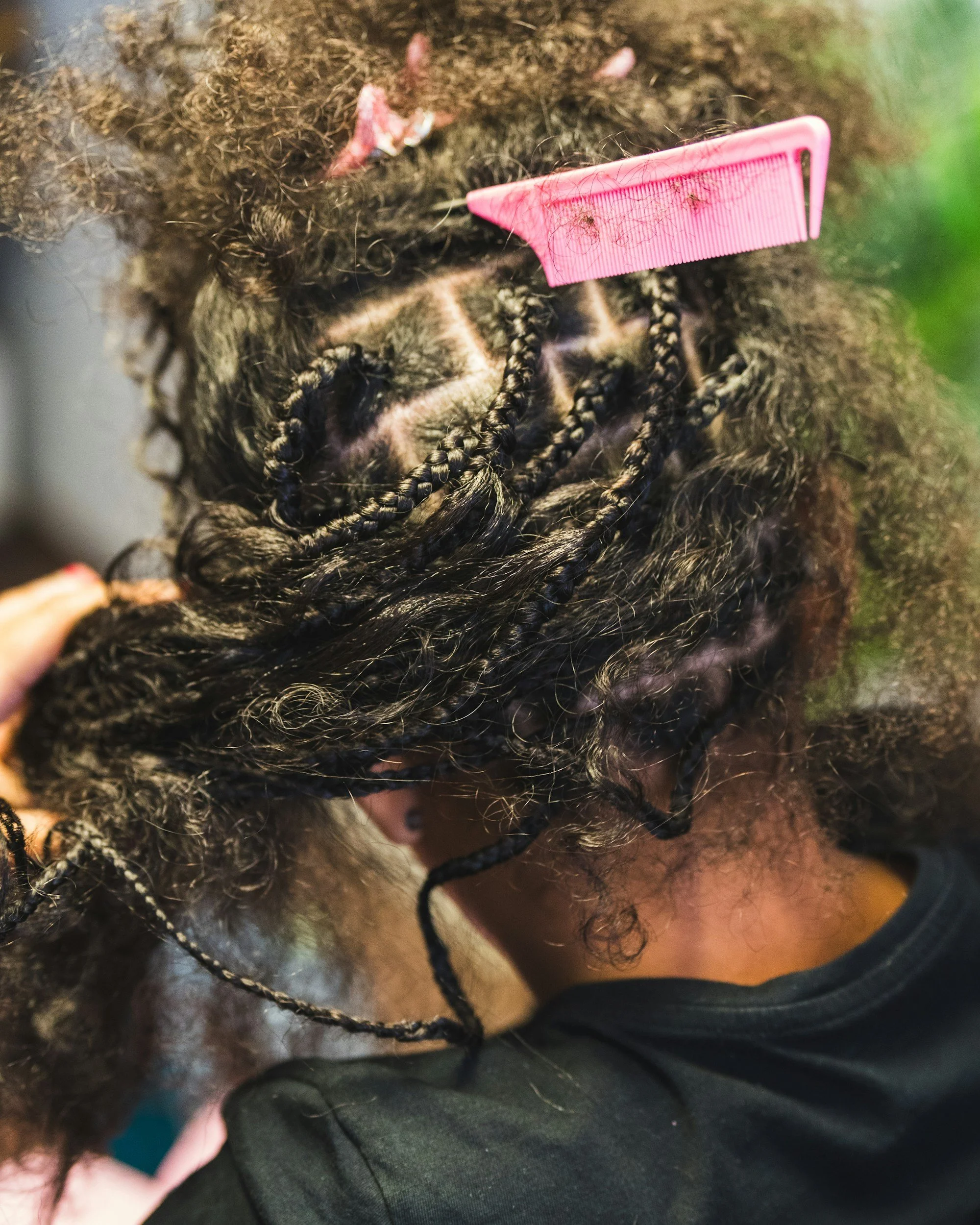 Close-up of a person's curly hair with a pink hair comb and some small hair sections.