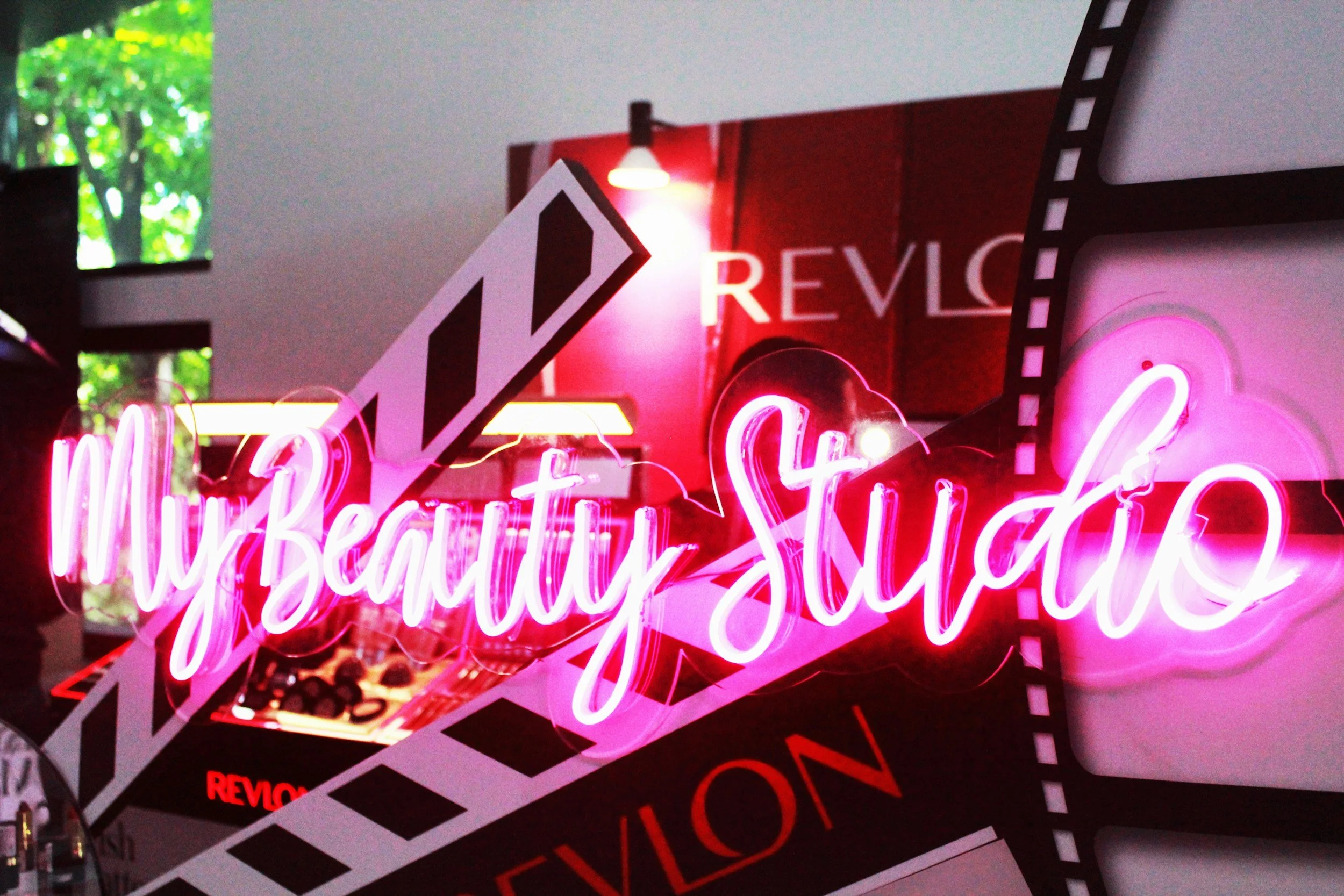 Bright pink neon sign spelling 'beautiful' with decorative elements, placed over other signs with red, white, and pink colors.