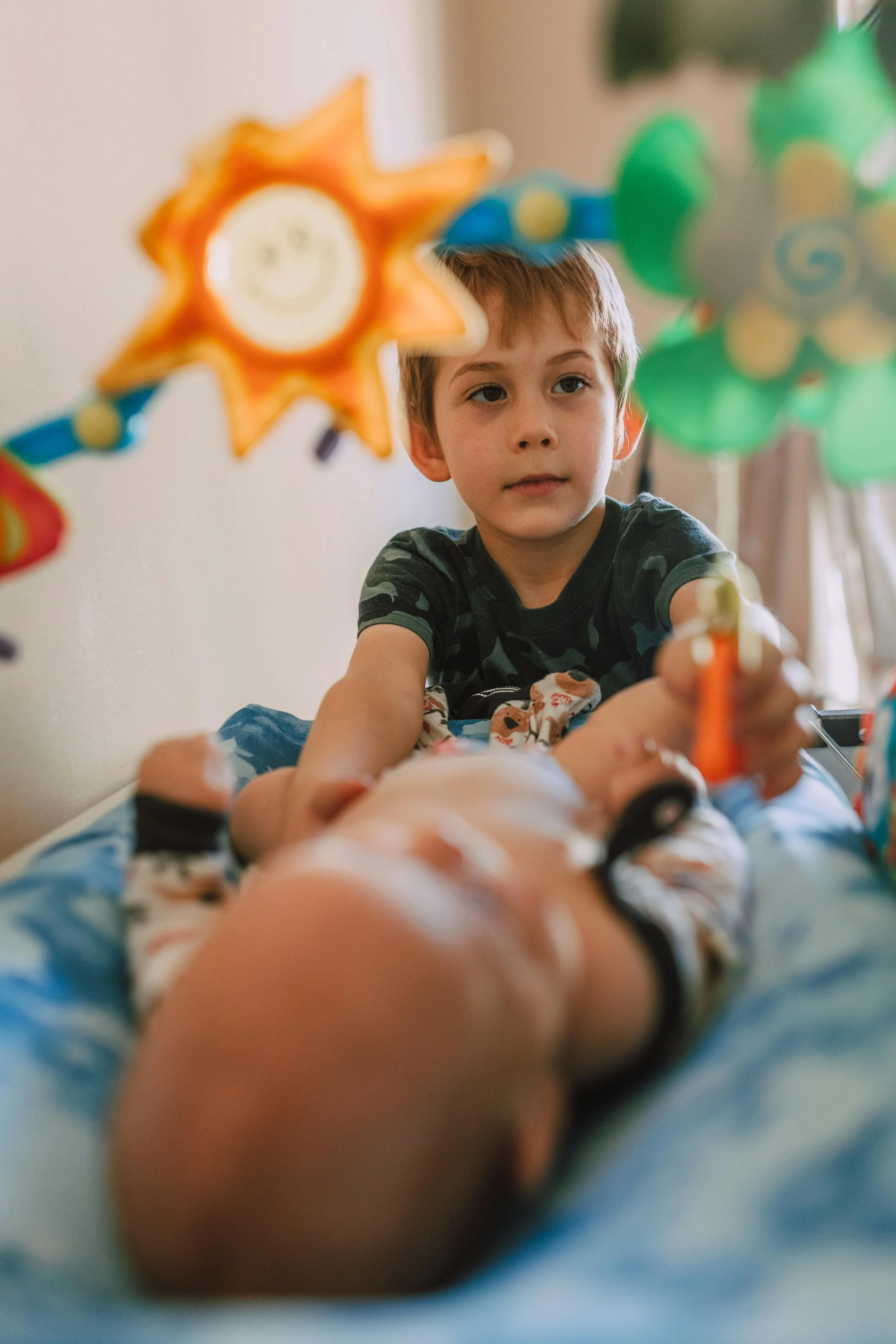 A young boy playing with colorful hanging toys on a bed.