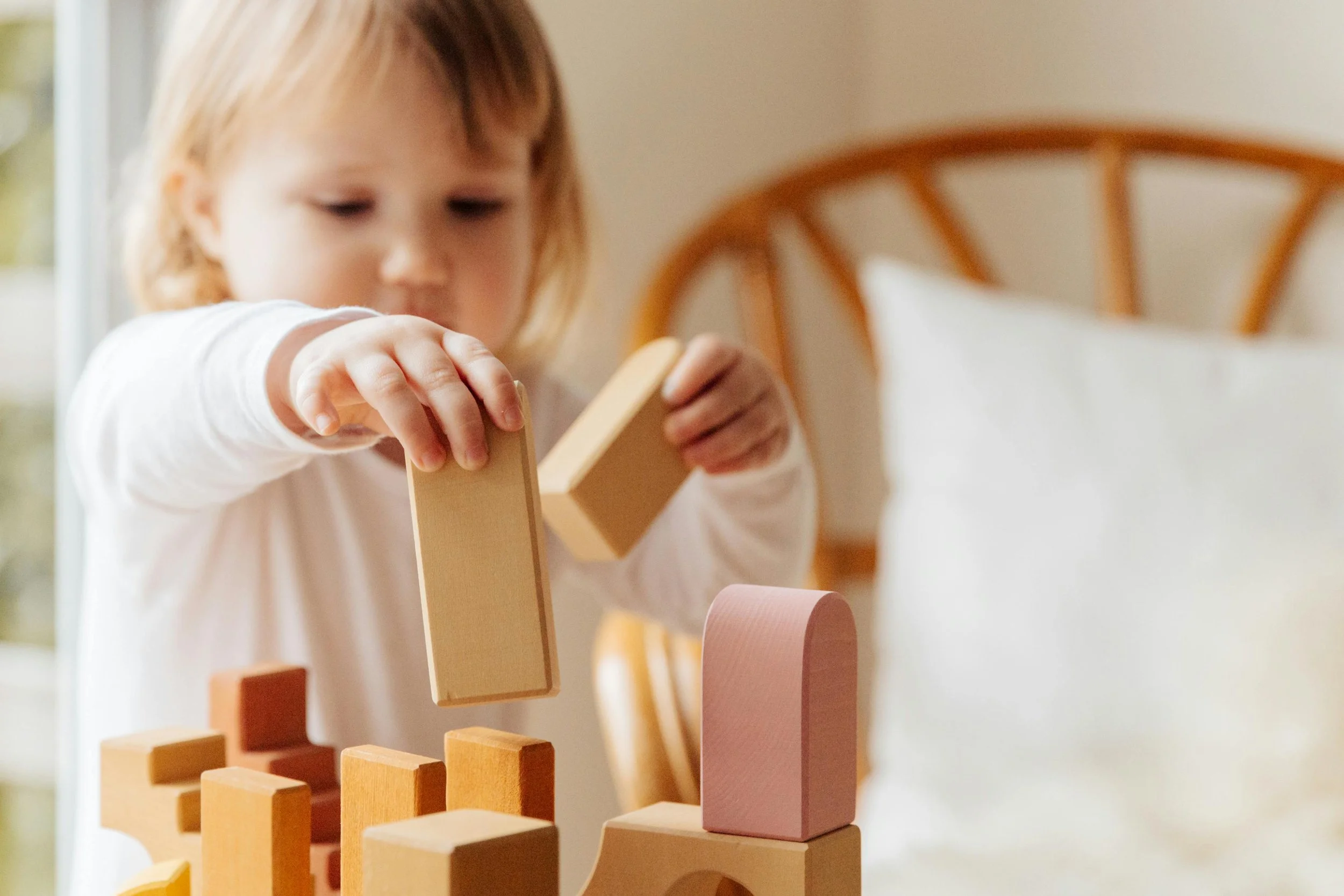 A young girl stacking wooden blocks of different shapes and colors on a bed.