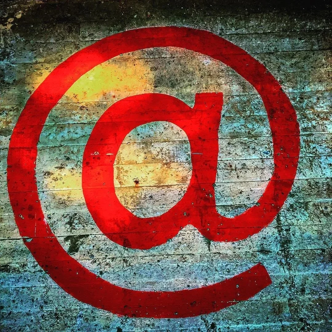 A large red 'at' symbol (@) painted on a weathered wooden surface.