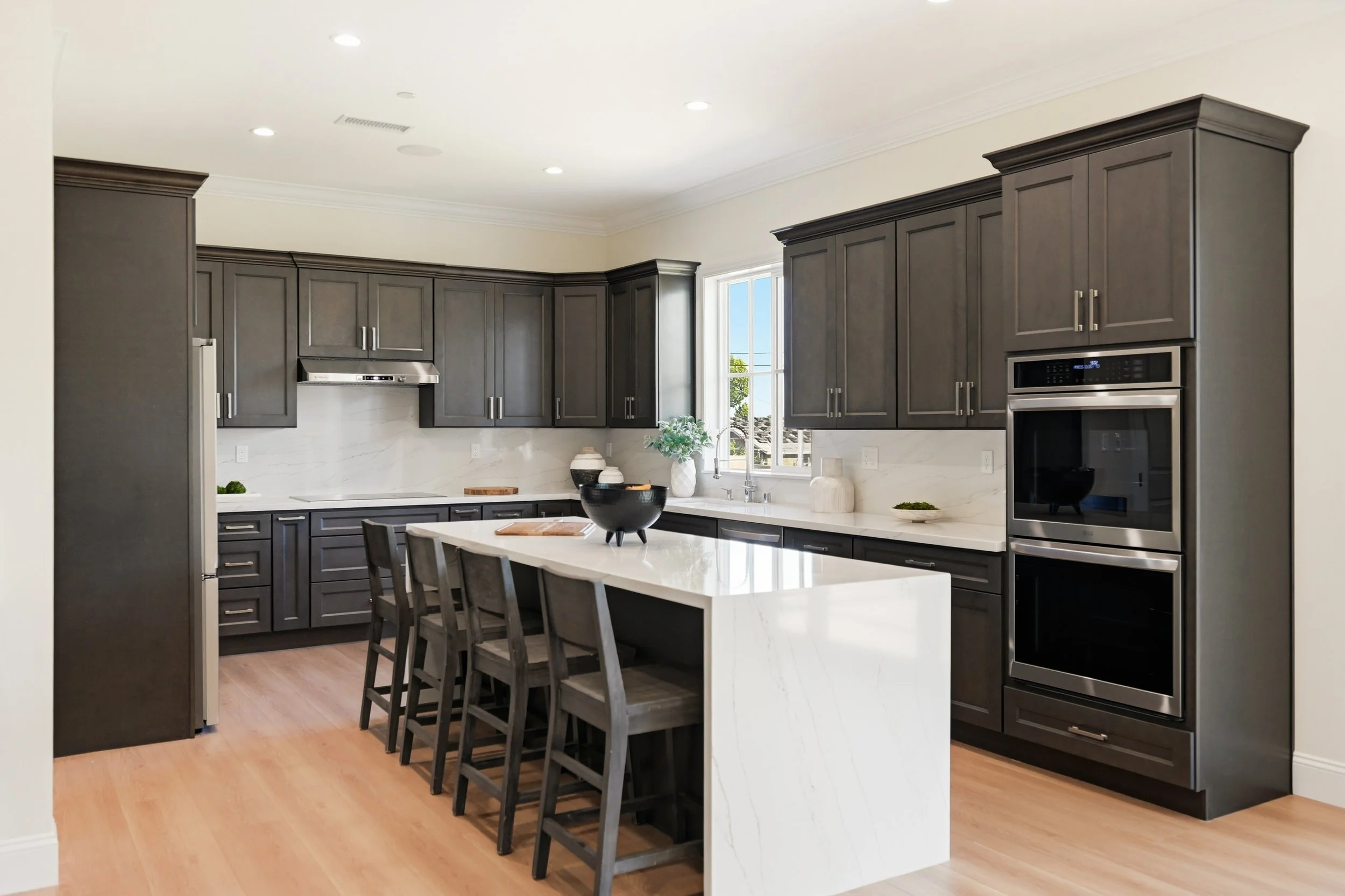 Modern kitchen with gray cabinets, white marble island, stainless steel appliances, and natural light from a window.