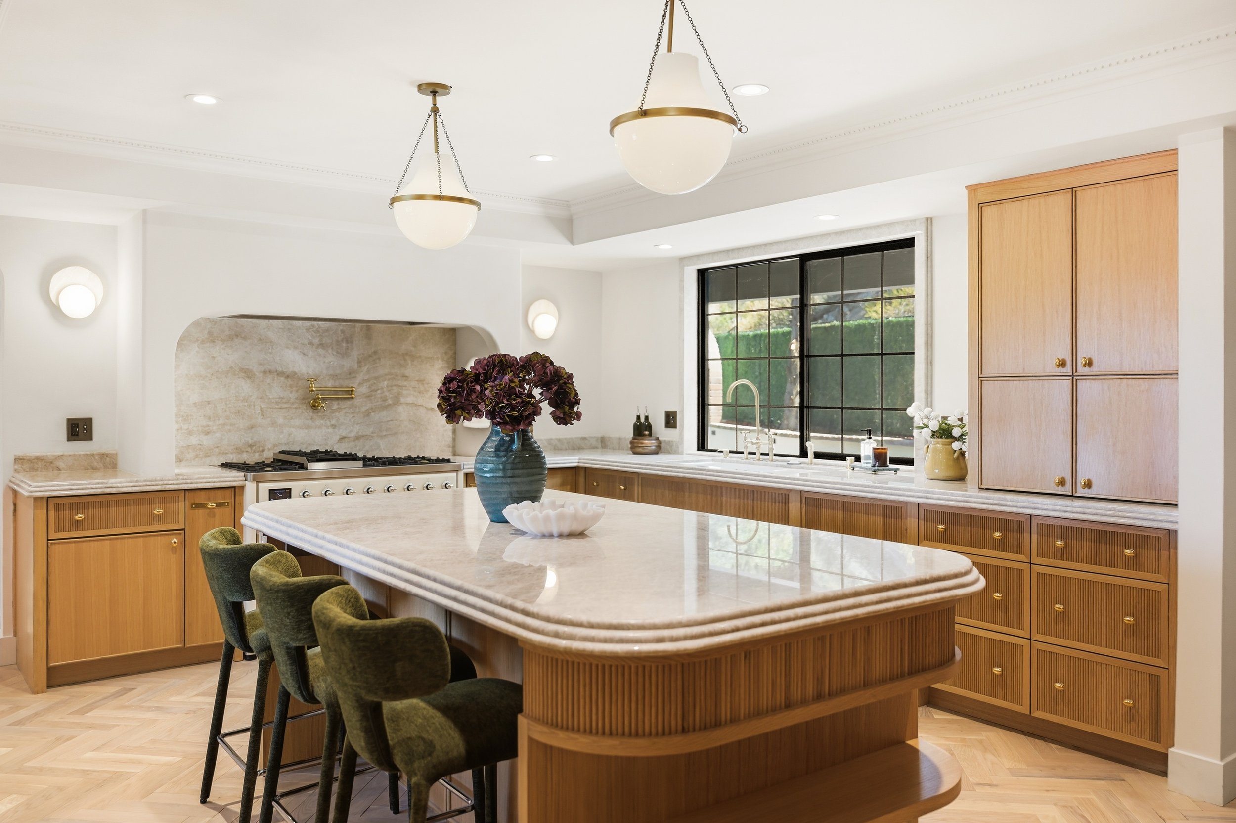 Modern kitchen with light wood cabinets, a marble island, black window frames, and pendant lights hanging from the ceiling.