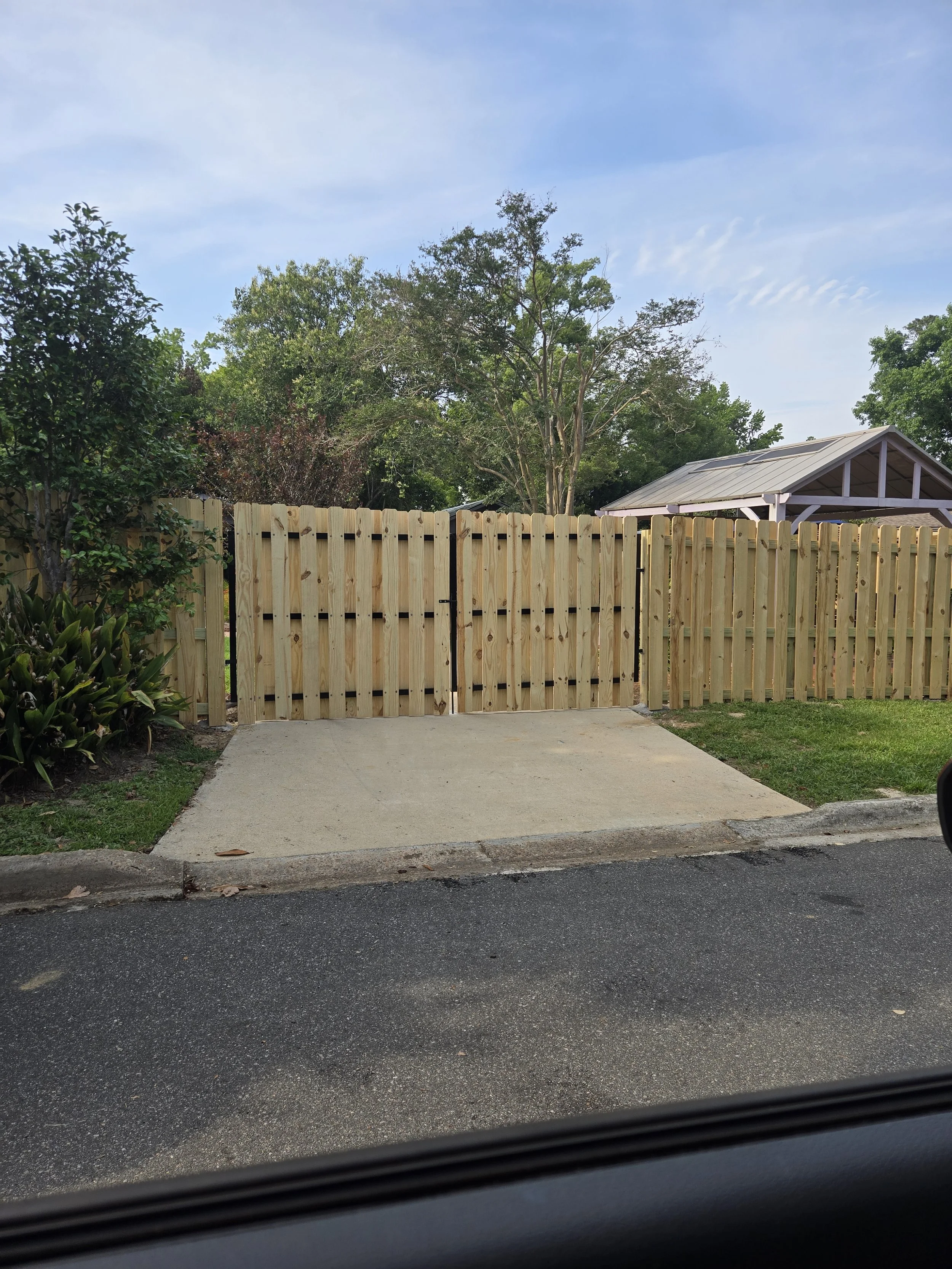 New wooden fence gate and fencing in a backyard with trees and clear sky.