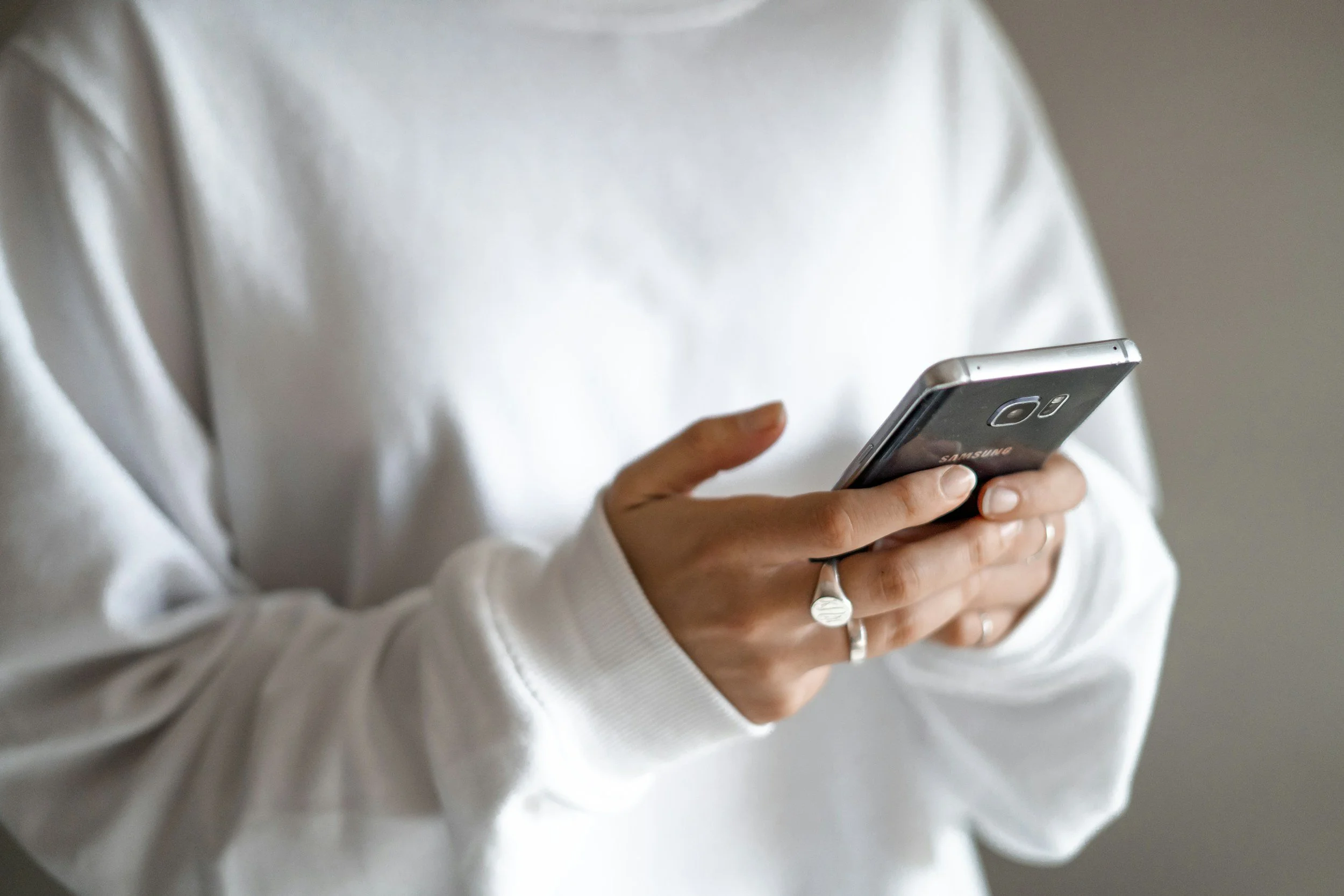 a women in white sweatshirt holding a cell phone with rings on, only her shirt and hands are visible,  therapy for attachment issues in fort collins, colorado, hannah dorsher