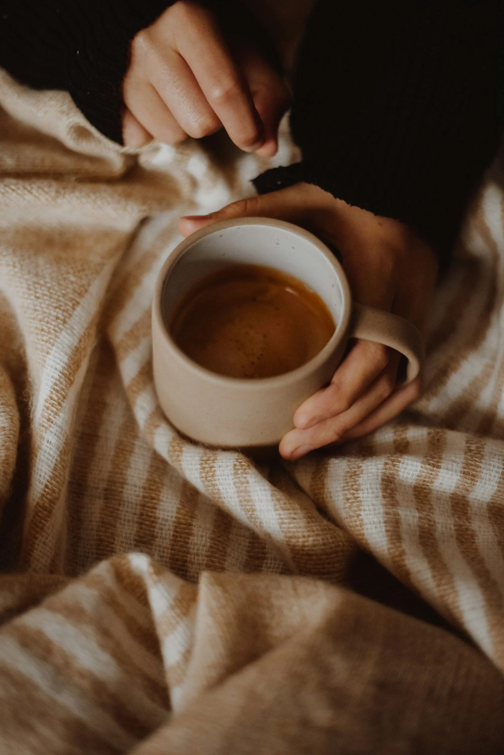 a women holding a coffee mug over a tan, striped blanket, therapy for trauma in fort collins colorado