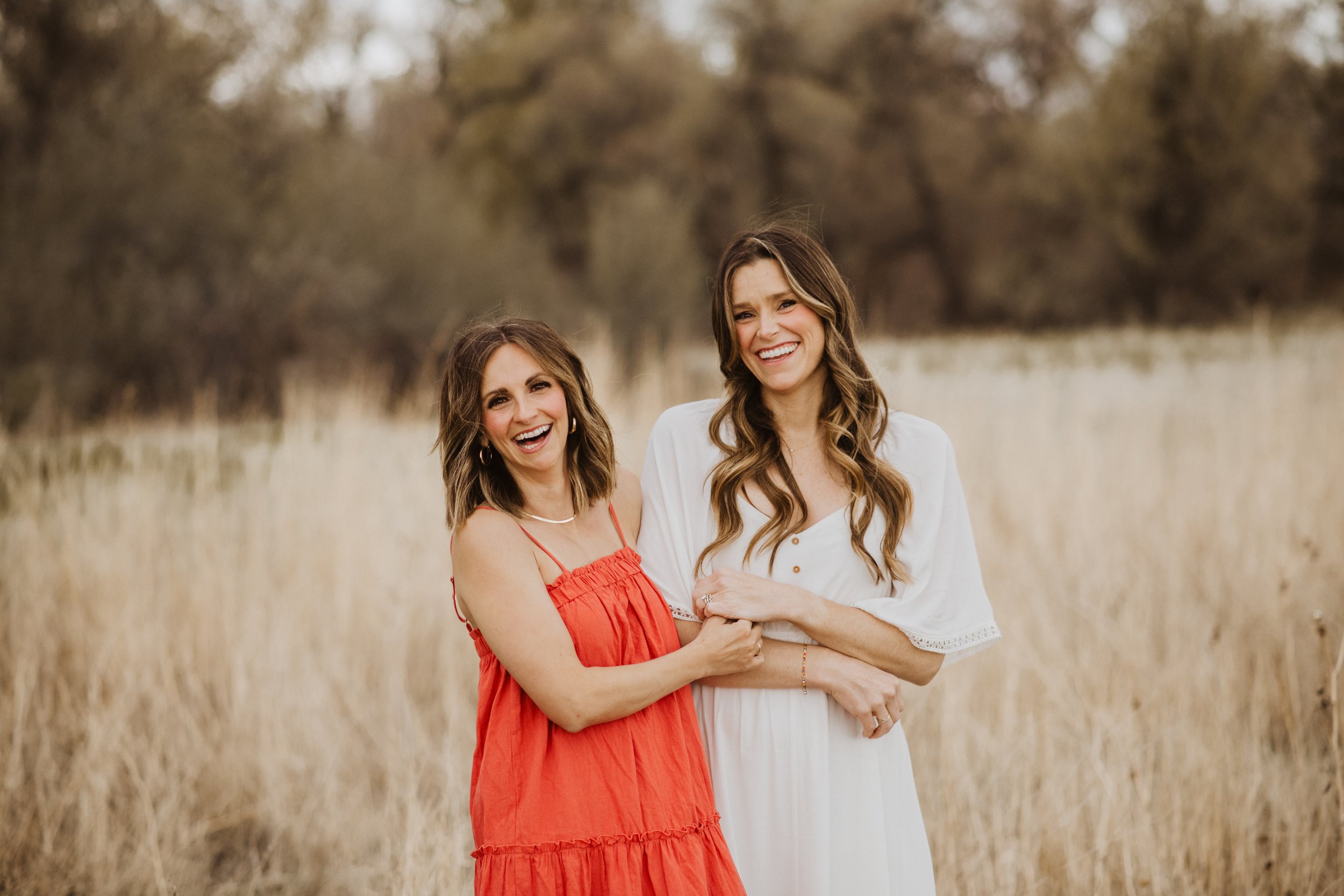 Kelly Sinning and Hannah Dorsher, two therapists for women and moms in fort collins colorado, holding hands and smiling in a field, in dresses
