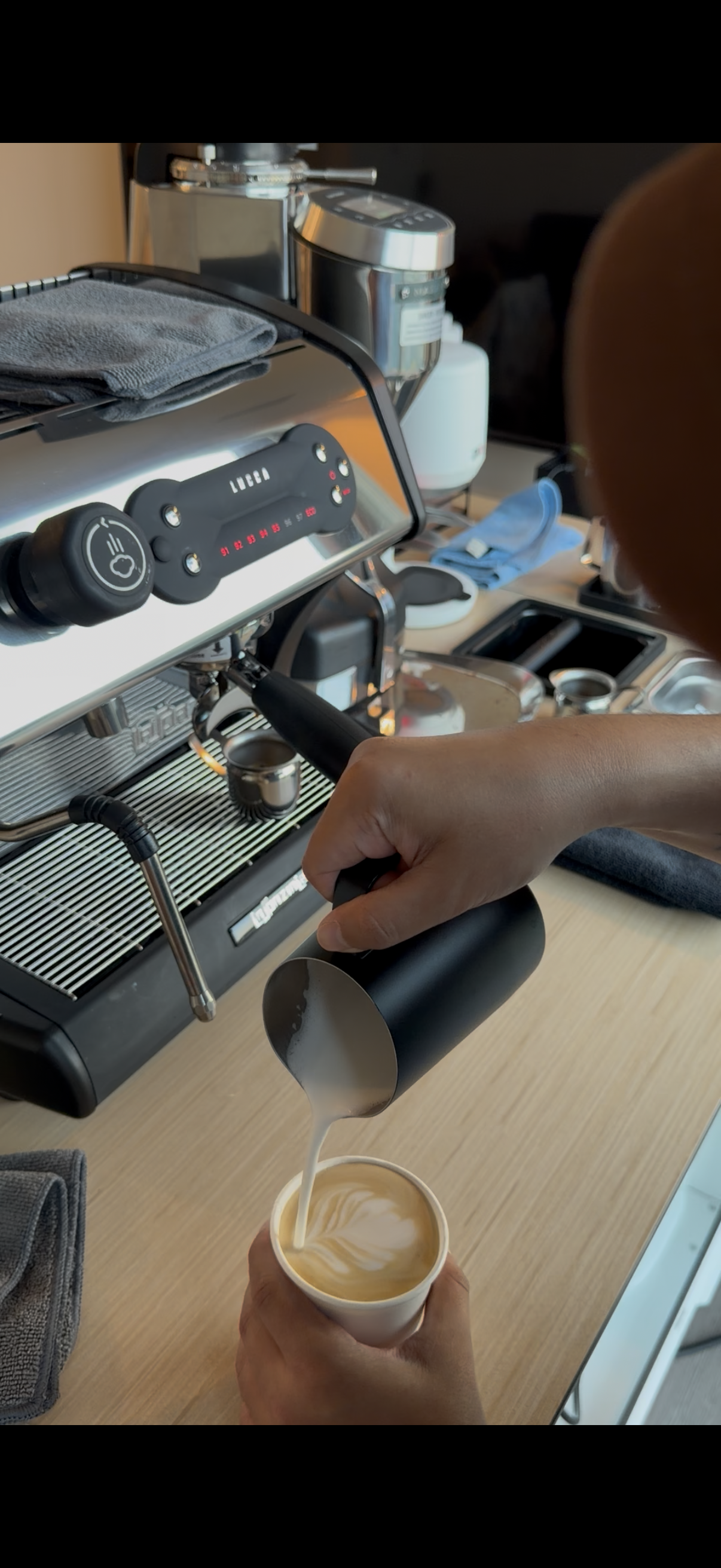 Barista making a hot latte with tulip latte art.
