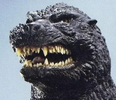 Close-up of a Godzilla figure or sculpture showing its head with sharp teeth and rough, scaly skin.