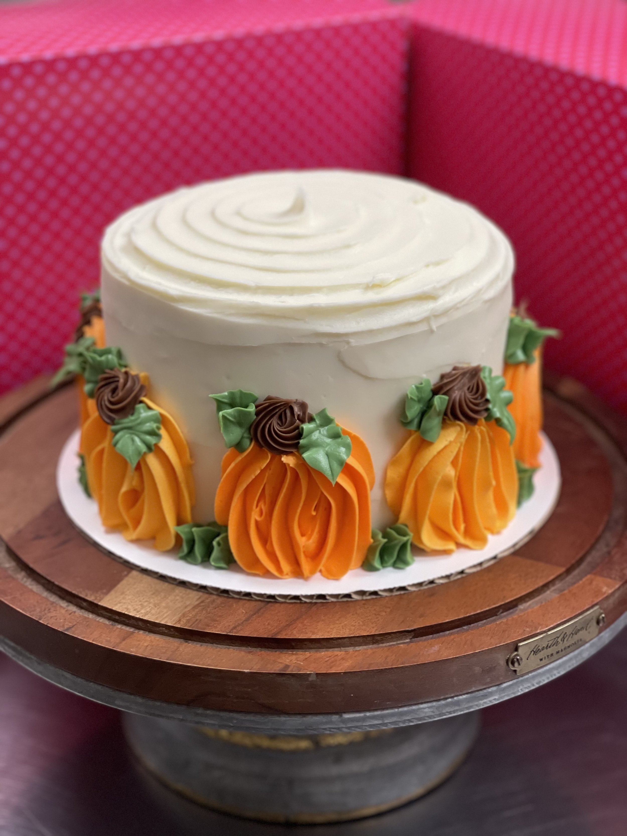 A round white frosted cake decorated with orange and green buttercream flowers on a wooden cake stand.