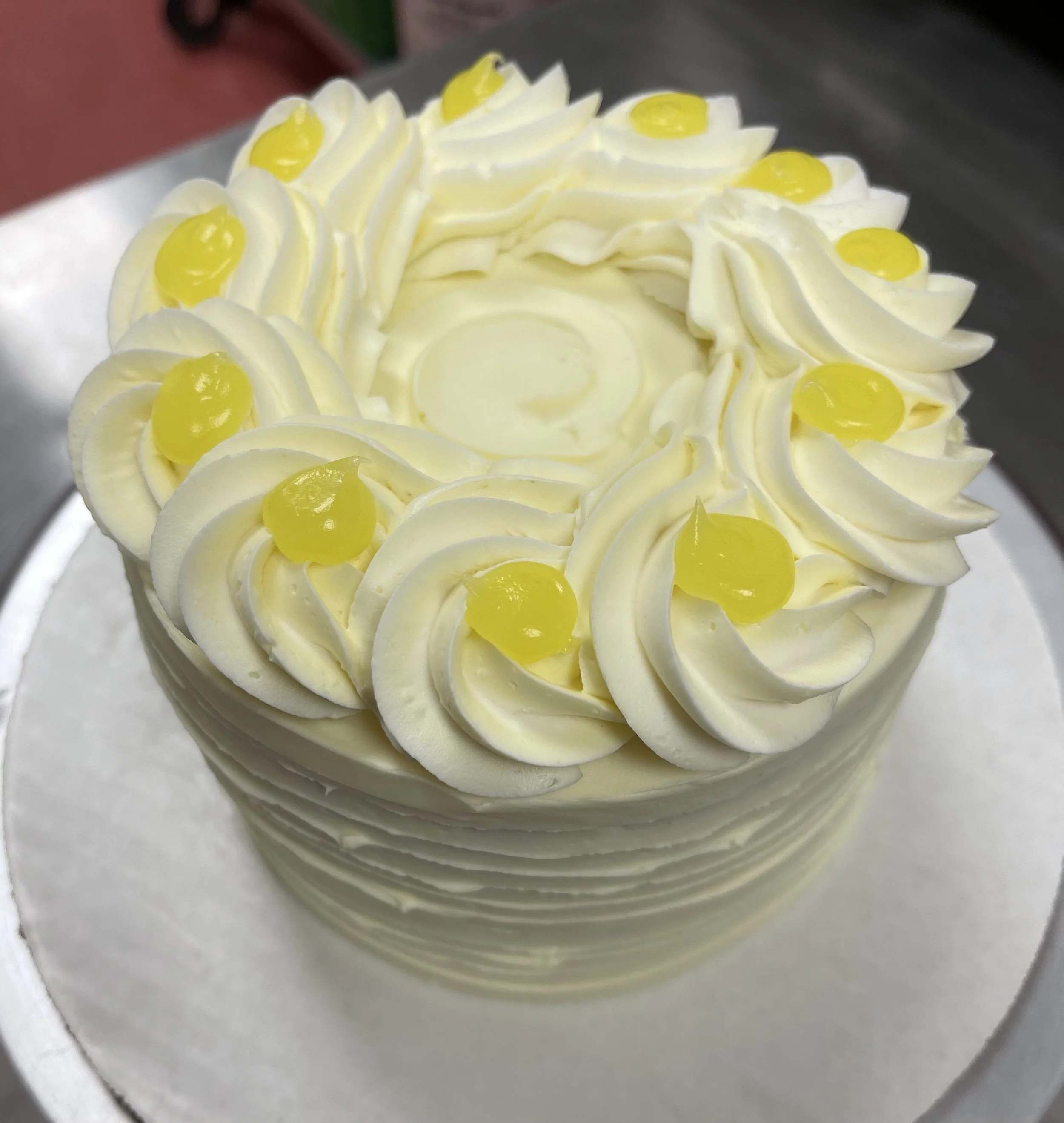 A round cake decorated with white frosting and yellow cherries on top, with a hollow center and layered cake sides.