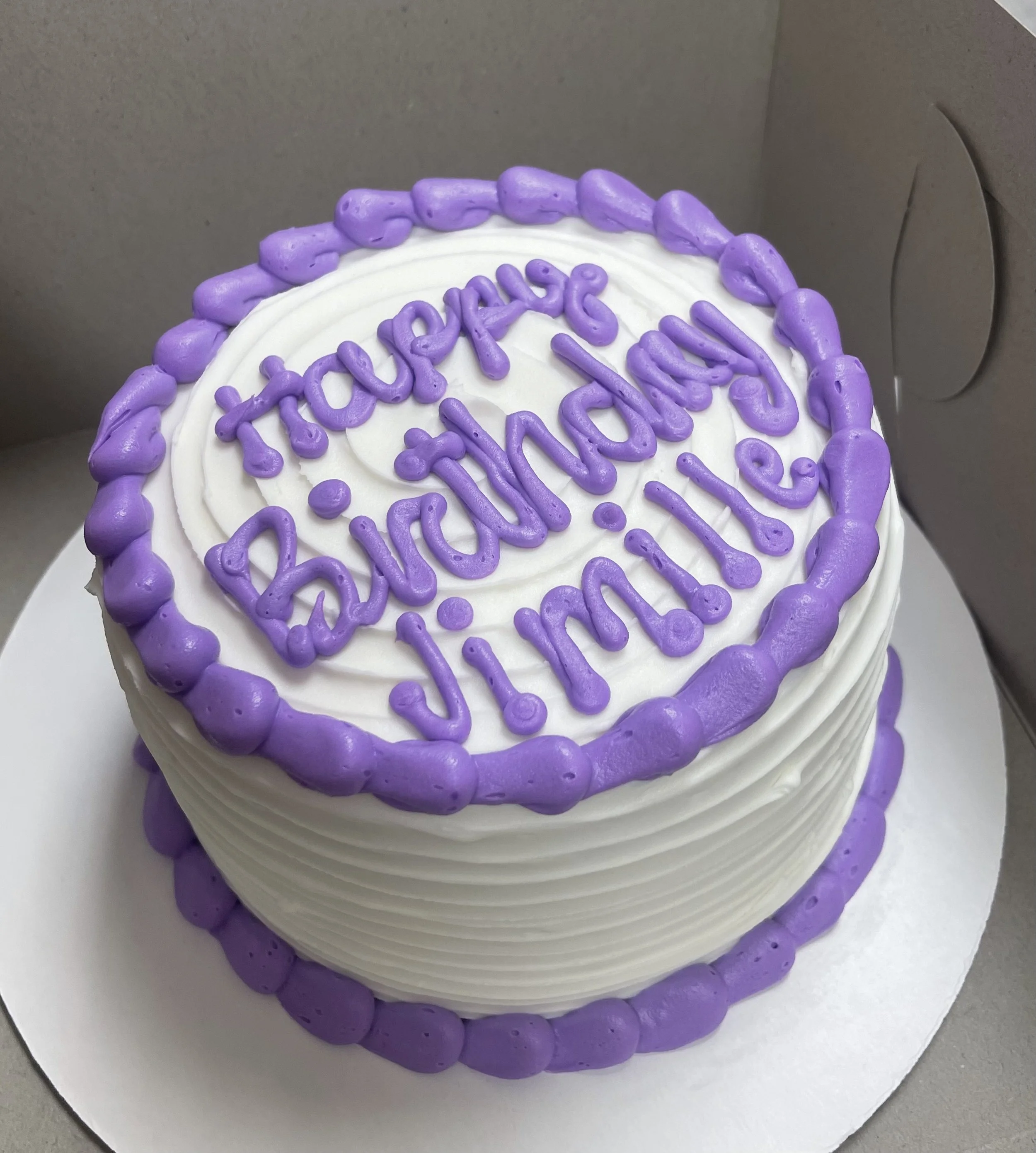 Round birthday cake with white frosting, purple border decorations, and purple writing on top that says 'Happy Birthday Julian'.