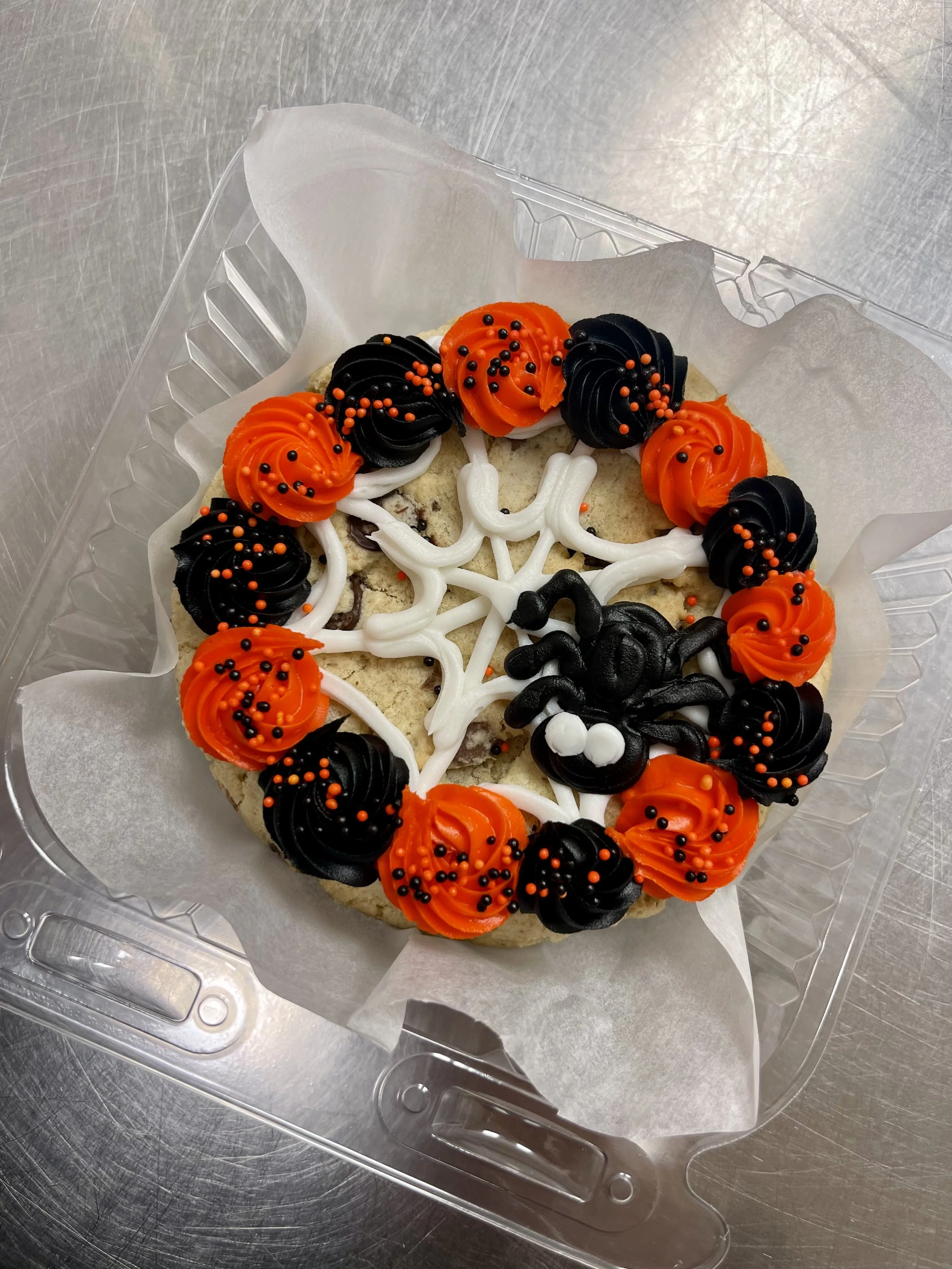 Halloween-themed cookie decorated with black and orange frosting, sprinkles, and a spider and spider web design.