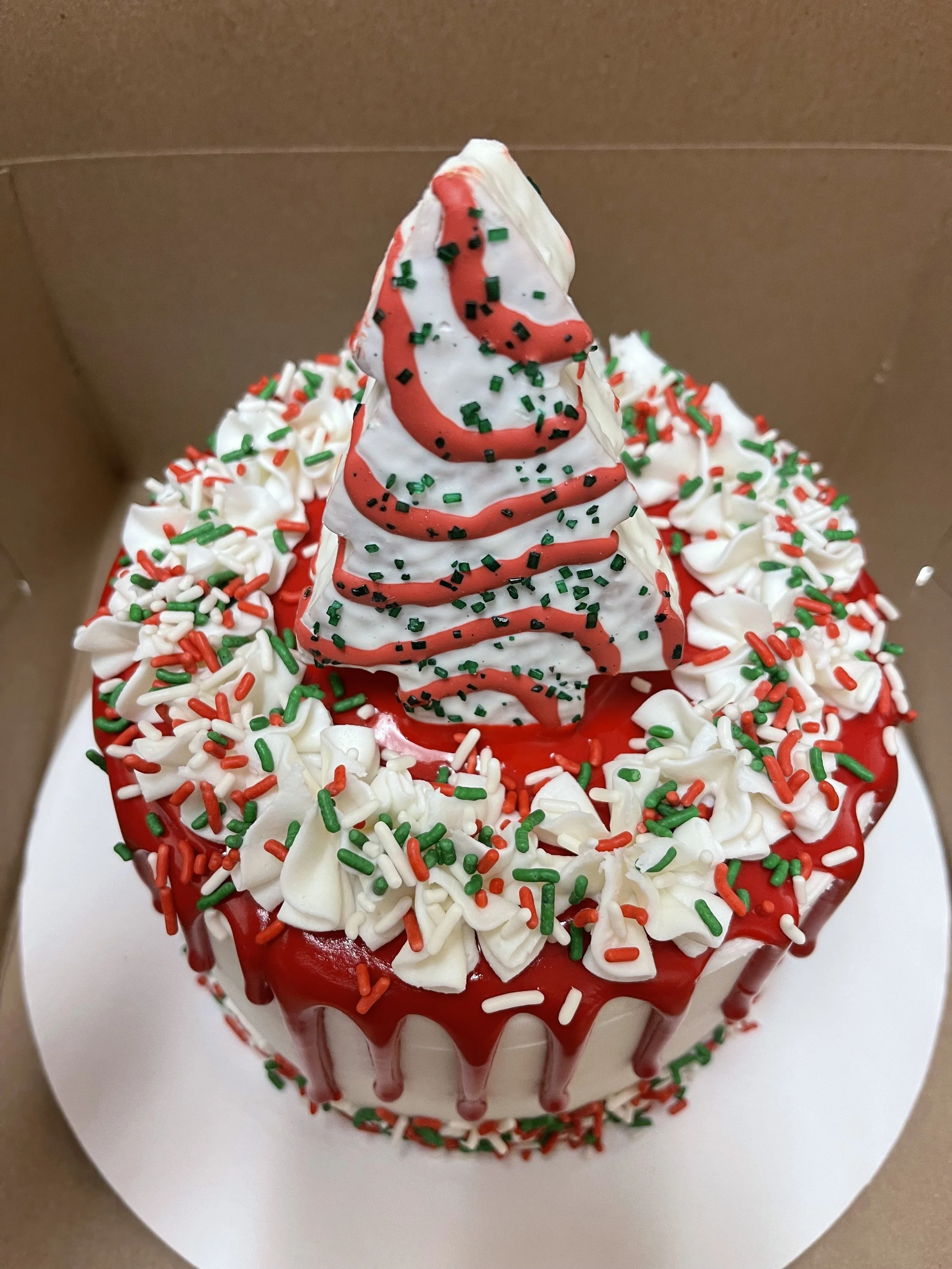 Christmas-themed cake with white icing, red and green sprinkles, and a whipped cream swirl topped with red and green sprinkles.