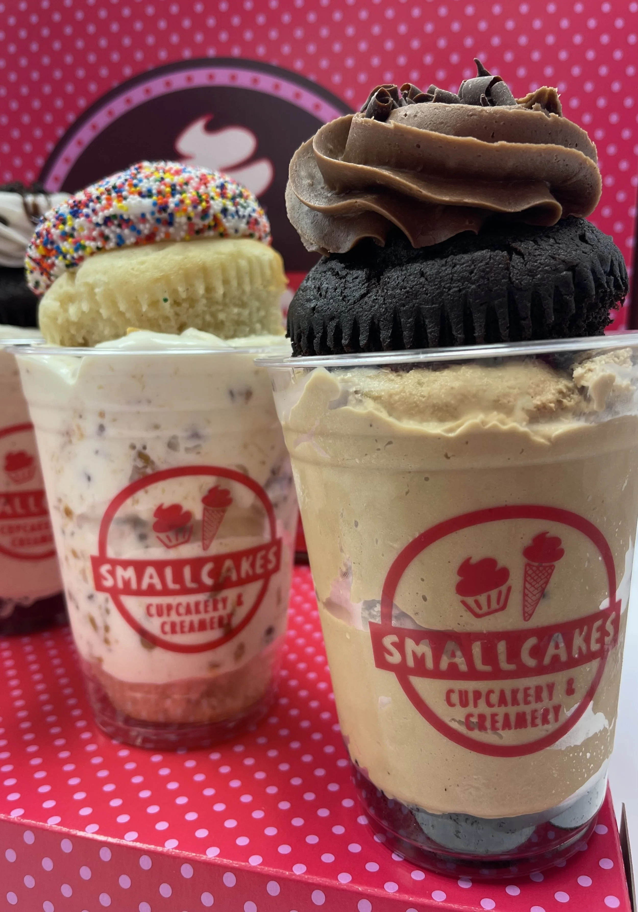 Various ice cream sundaes and cupcakes from Smallcakes Cupcakery & Creamery displayed on a pink polka dot box.