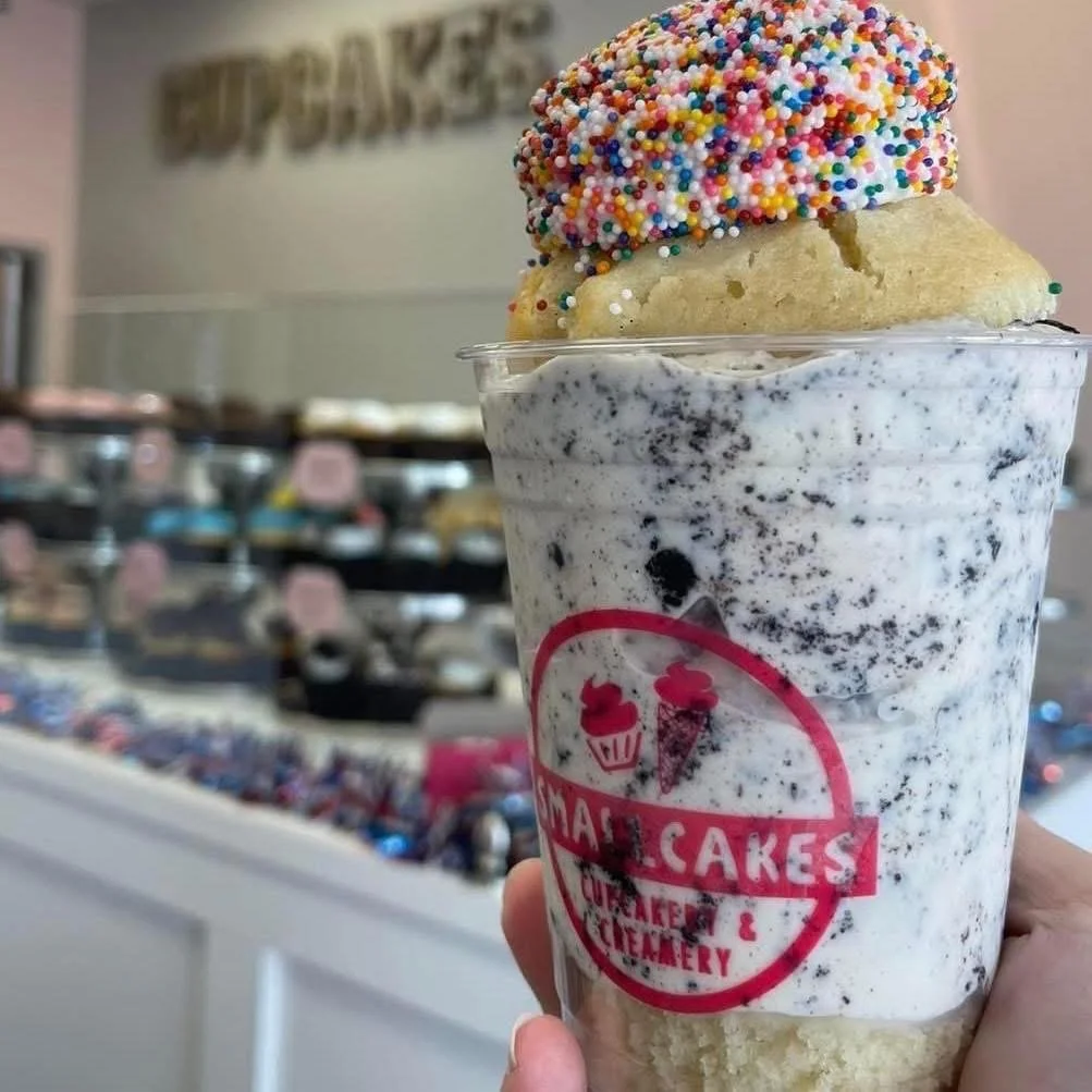A large cup of cookies and cream ice cream topped with a donut covered in colorful sprinkles.