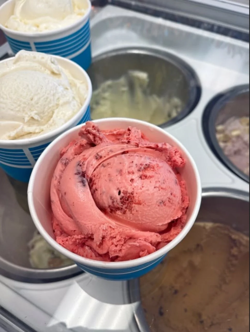 Three cups of different flavored ice cream in a freezer with other ice cream containers.