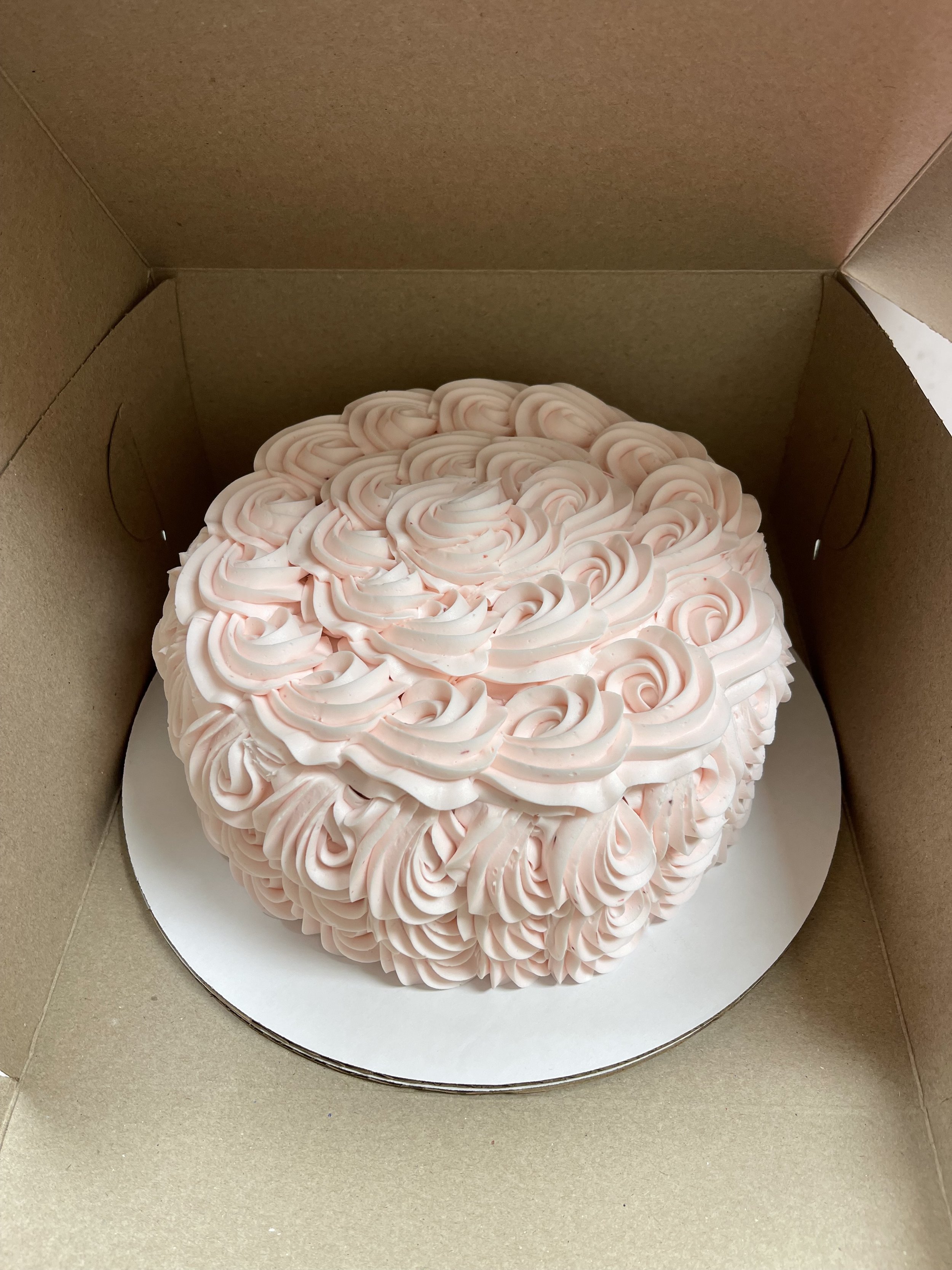 A pink cake with rosette frosting inside a cardboard box.