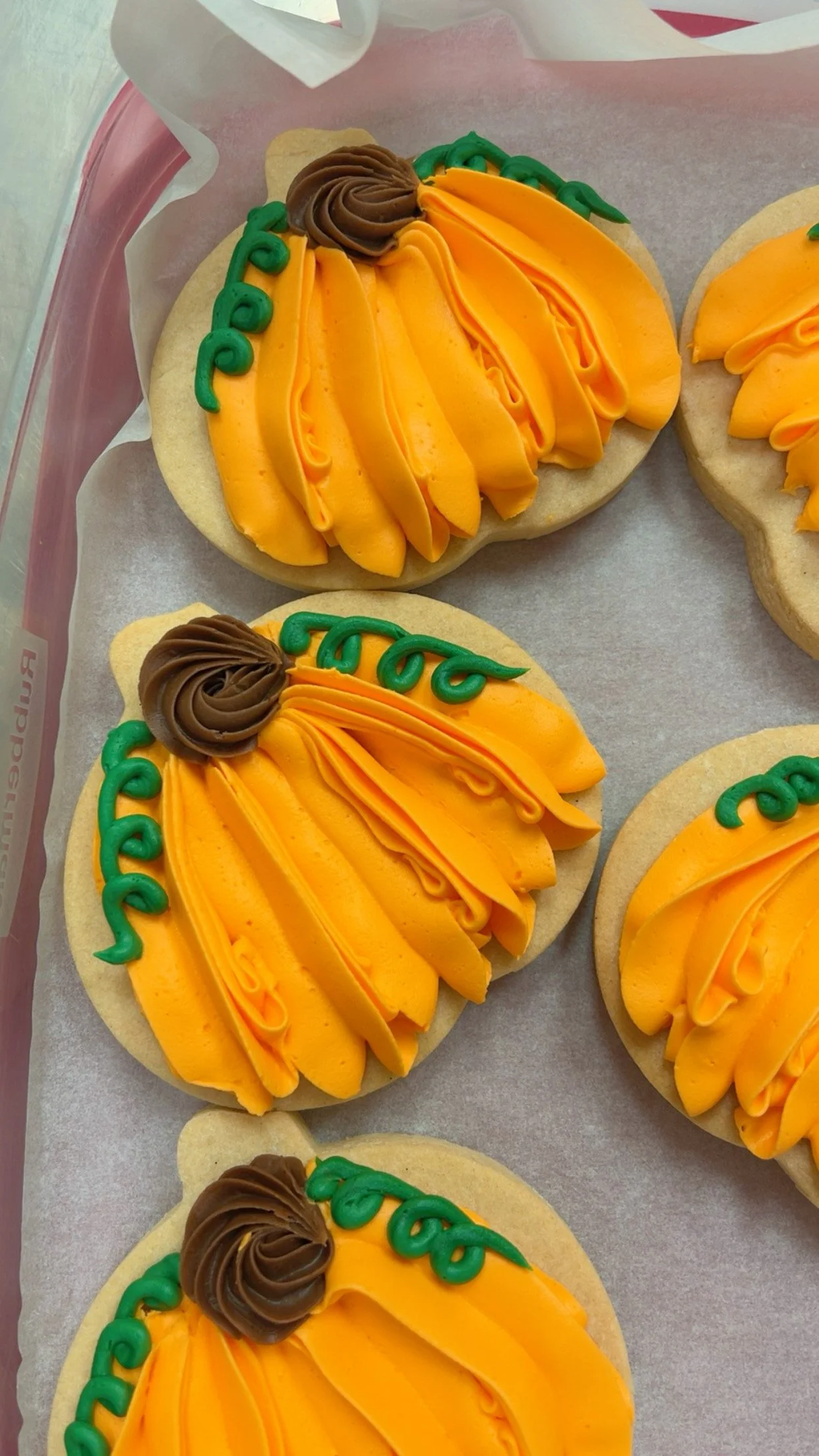 Sugar cookies decorated with orange and yellow frosting to resemble pumpkins, with green icing for leaves, and a brown frosting swirl on top.