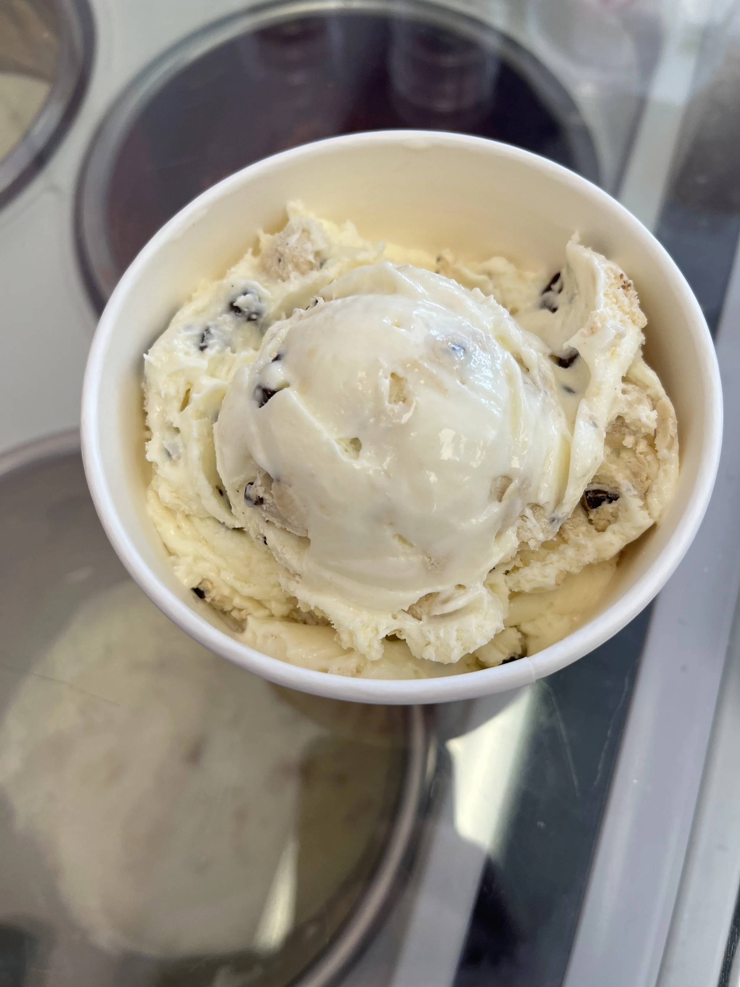 A cup of vanilla ice cream with chocolate chips on top, placed over an ice cream freezer.